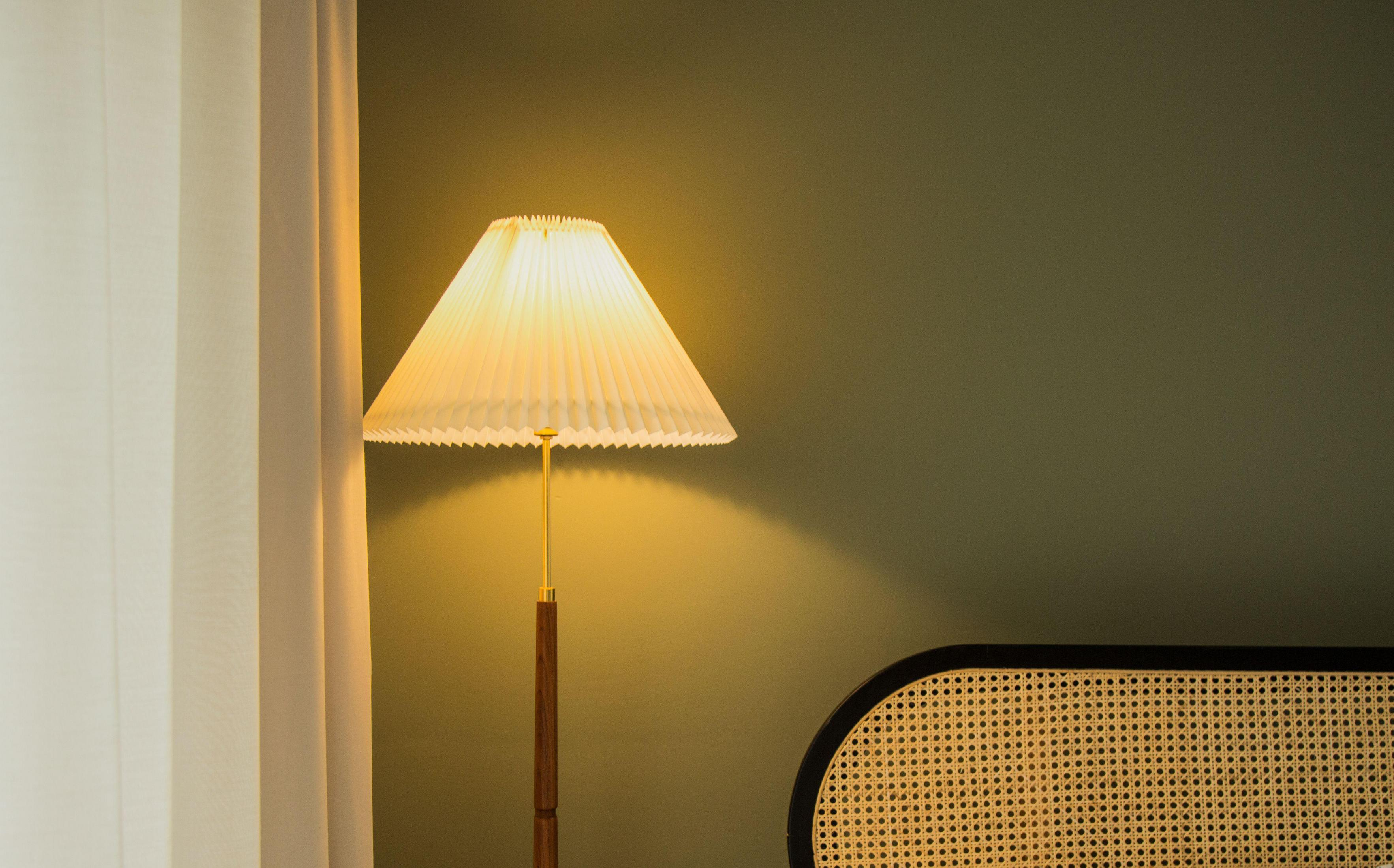 Zapalona lampa z plisowanym abażurem stoi obok białej zasłony i zielonej ściany.
