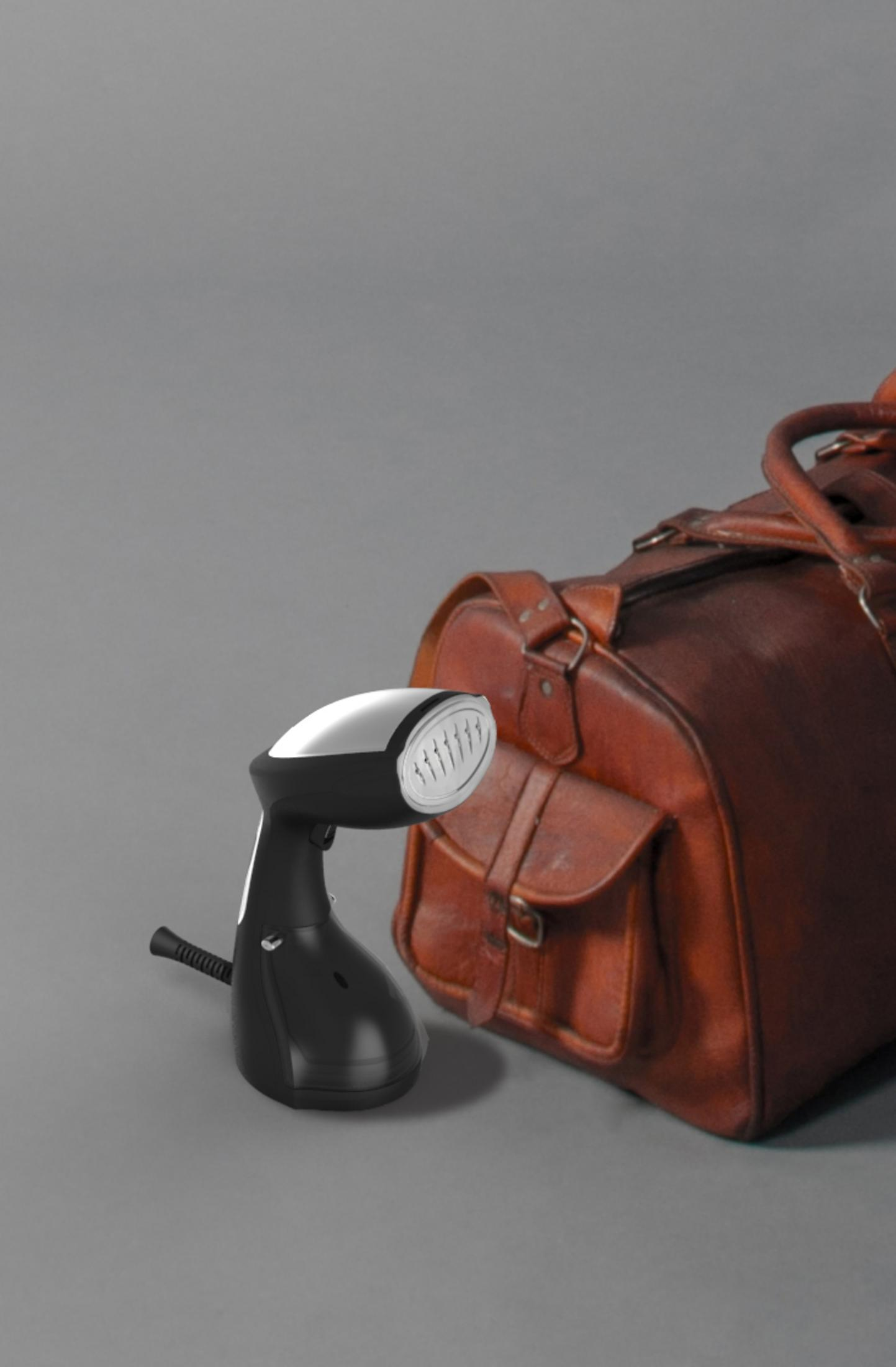 Défroisseur à côté d'un sac de voyage en cuir marron, surface grise.