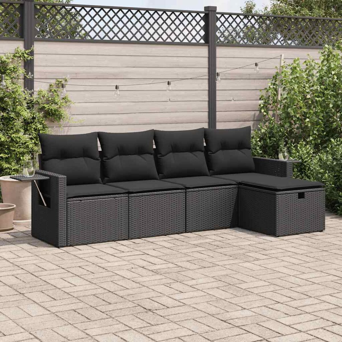 Dunkelgraues Rattan-Sofaset mit schwarzen Kissen, auf einer Backstein-Terrasse, mit Beistelltisch.