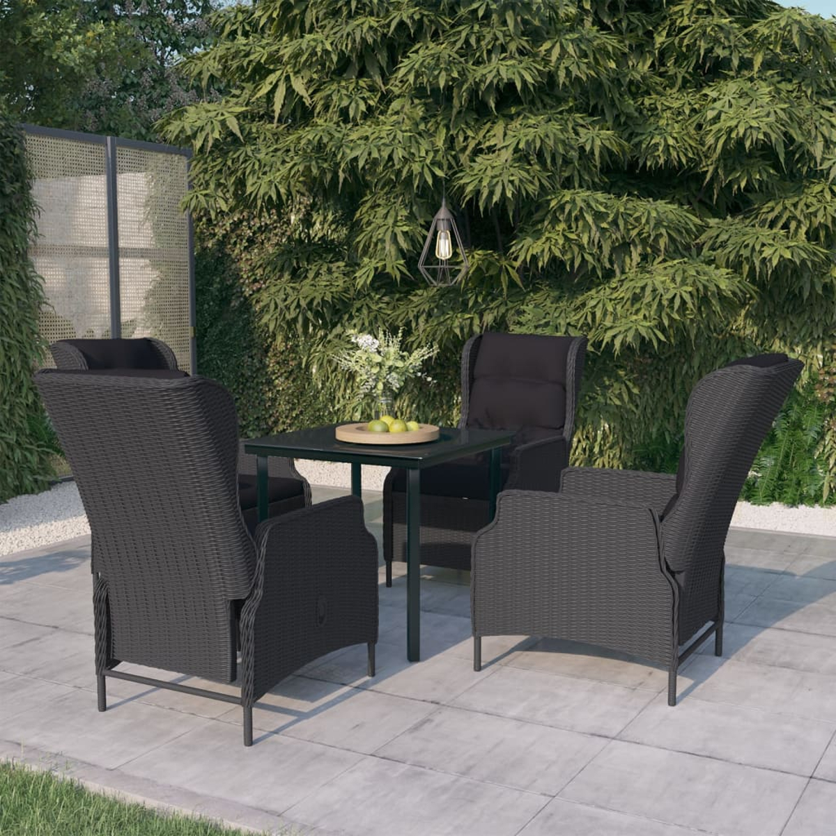 Vier dunkle Rattan-Stühle mit schwarzen Kissen um einen Tisch mit Obst auf einer Terrasse mit Grün.