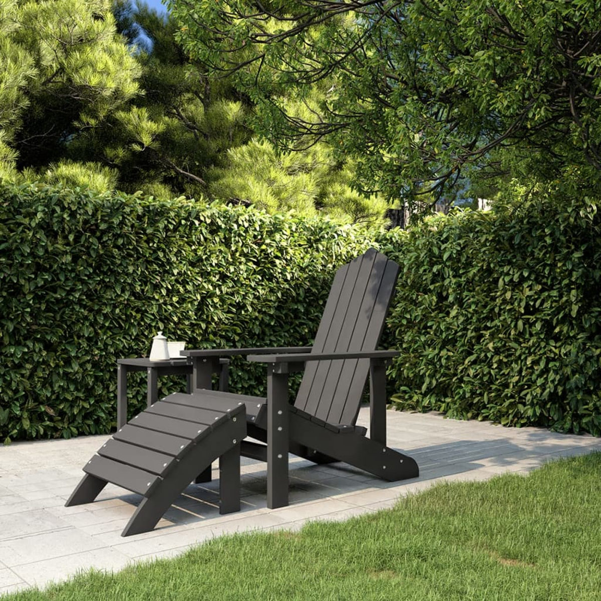 Grauer Adirondack-Stuhl mit Fußstütze auf einer Terrasse, mit Grün im Hintergrund.