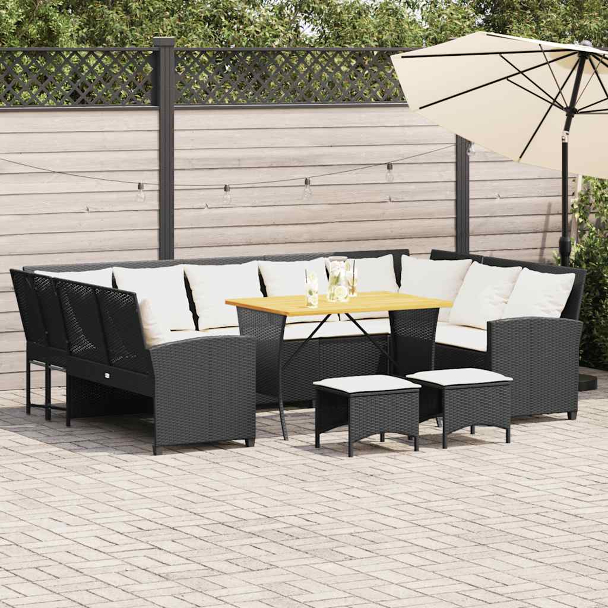 Ein schwarzes Korbgeflecht-Terrassenmöbel-Set mit weißen Kissen, Holztisch und Hockern.
