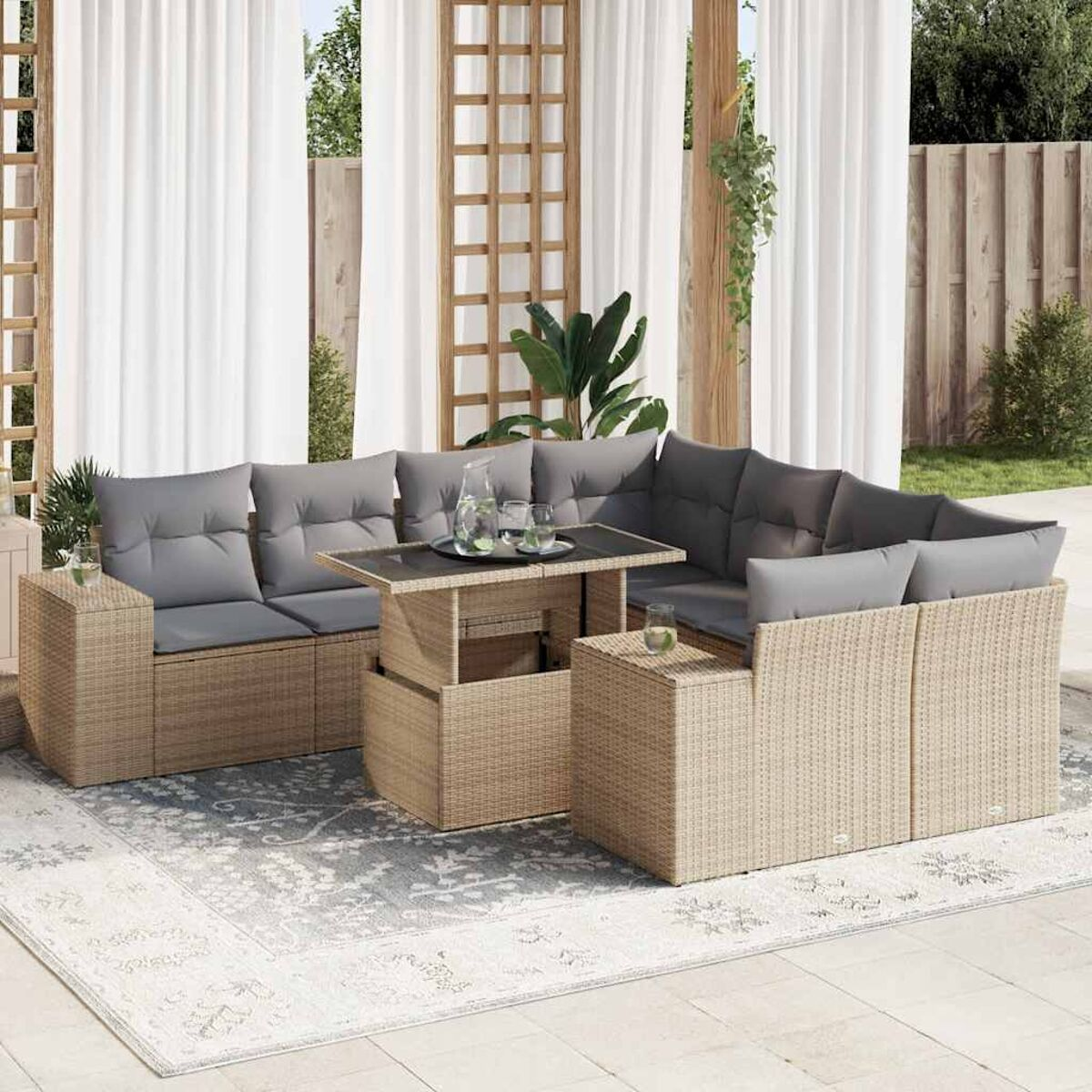 Set divano in rattan da esterno con cuscini, un tavolo e un tappeto. Lo sfondo è una tenda bianca.