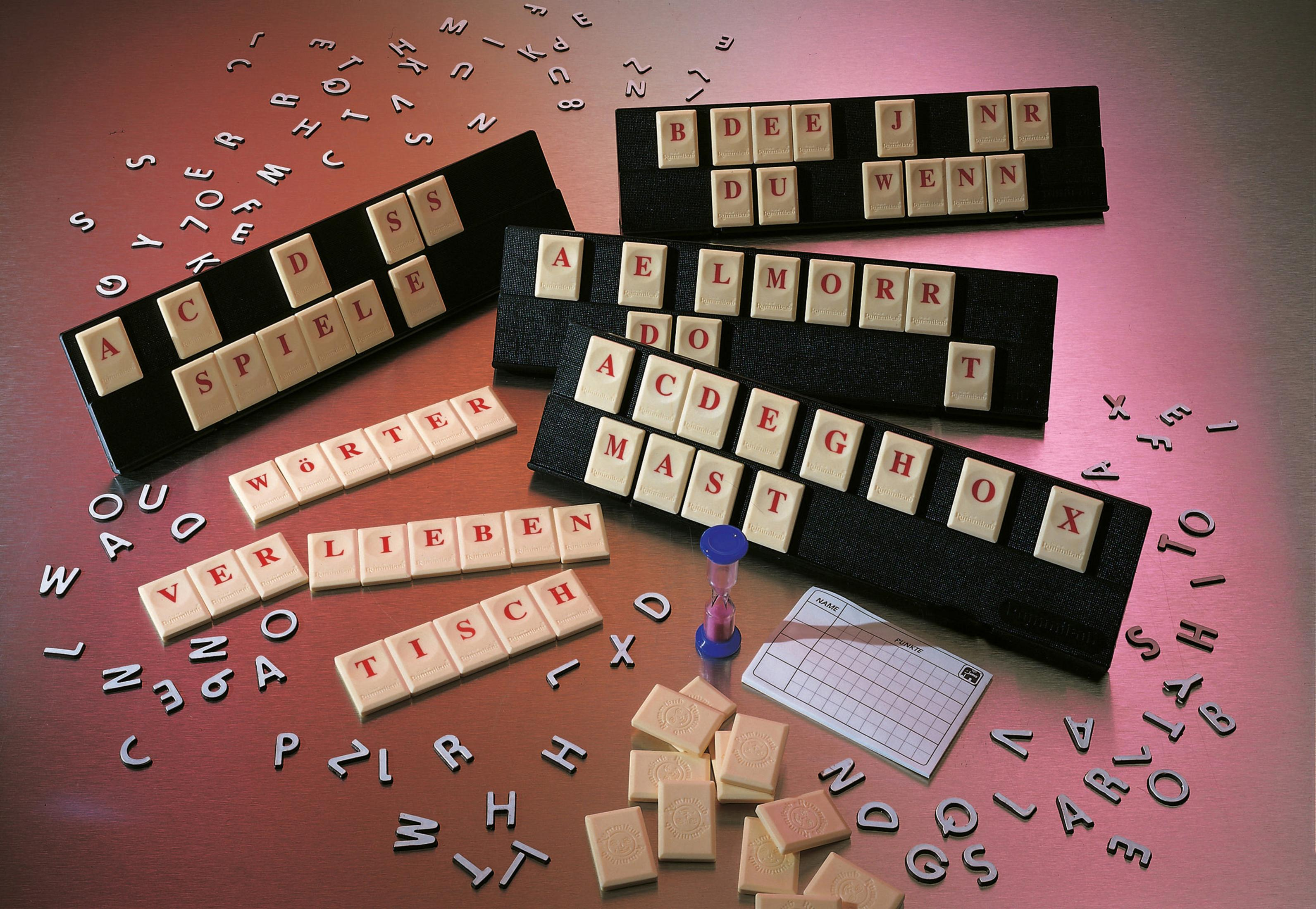 Rummikub-Spiel mit Kacheln, die Wörter auf schwarzen Haltern und losen Kacheln bilden.