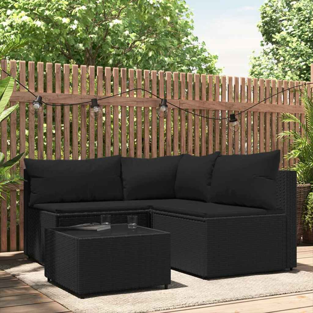 Schwarzes Rattan-Ecksofa mit Kissen und einem Tisch in einem Garten. Im Hintergrund ein Holzzaun.