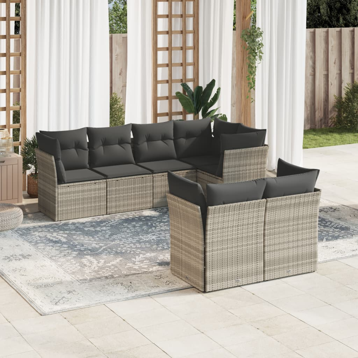 L-förmiges beiges Korbmöbelsofa mit dunkelgrauen Kissen auf einem blauen Teppich. Weiße Vorhänge und Terrasse.