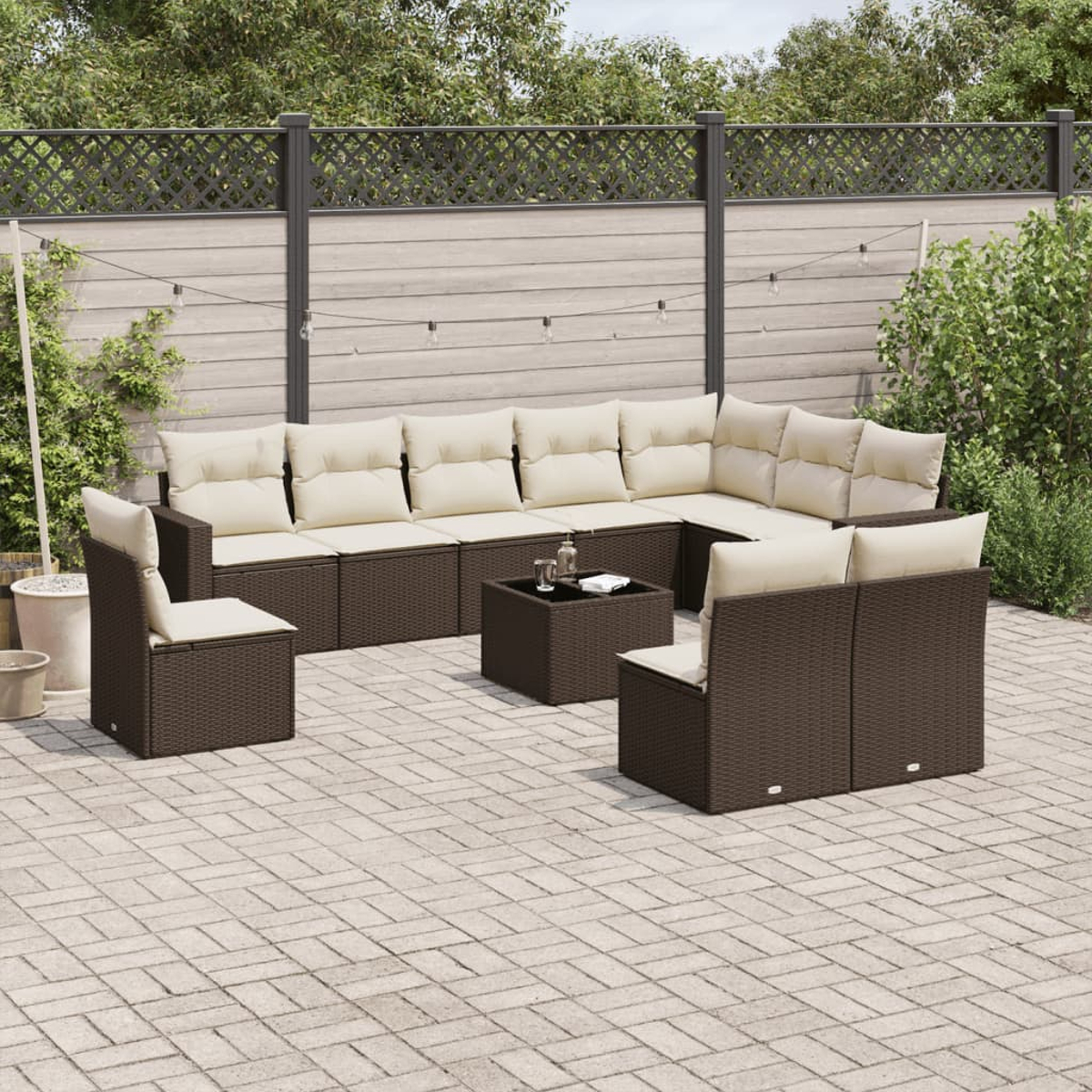 Divano componibile in vimini marrone da esterno, sedie e tavolino con cuscini beige su un patio.