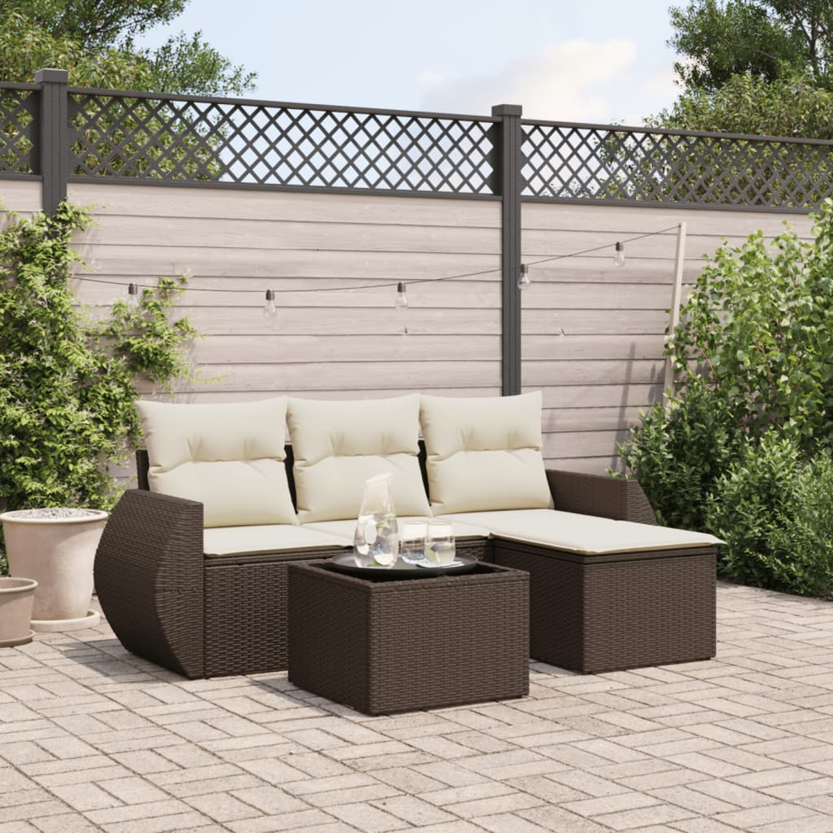 Set di mobili da esterno in rattan marrone. Include divano, tavolino e tavolino laterale. Sfondo: patio pavimentato.