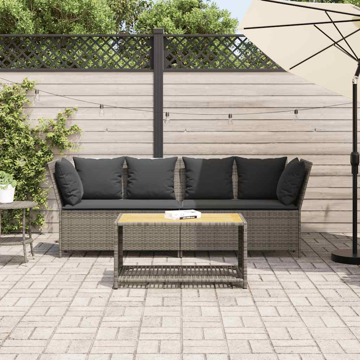 Divano in vimini grigio con cuscini neri e tavolino nero, su un patio con ombrellone color crema.
