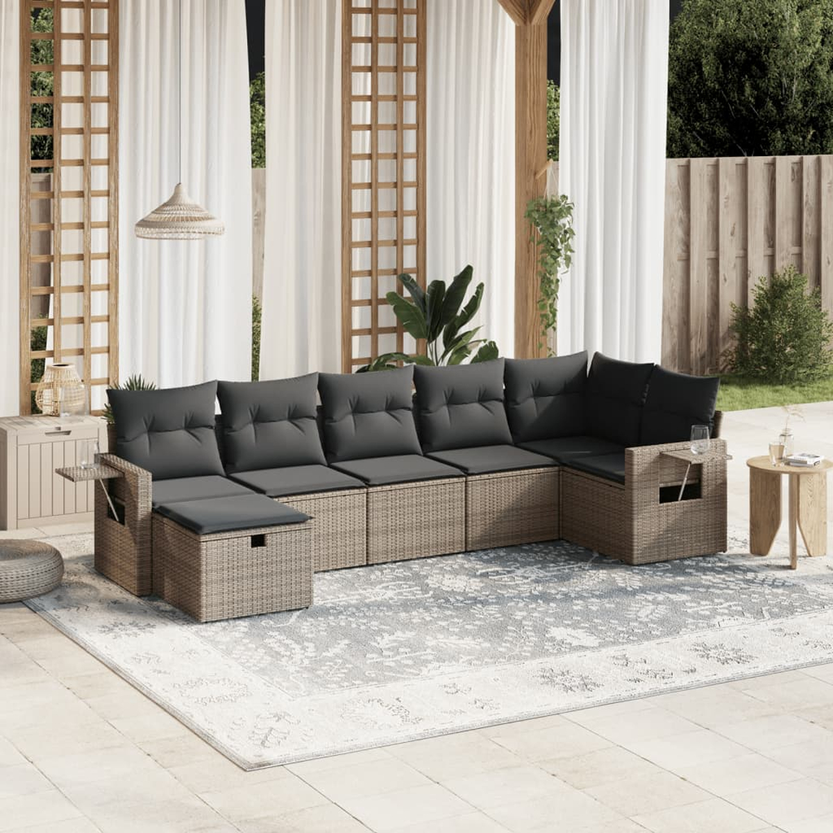 Graue Rattan-Gartengarnitur mit schwarzen Kissen und einem Teppich. Holztisch und Vorhänge im Hintergrund.