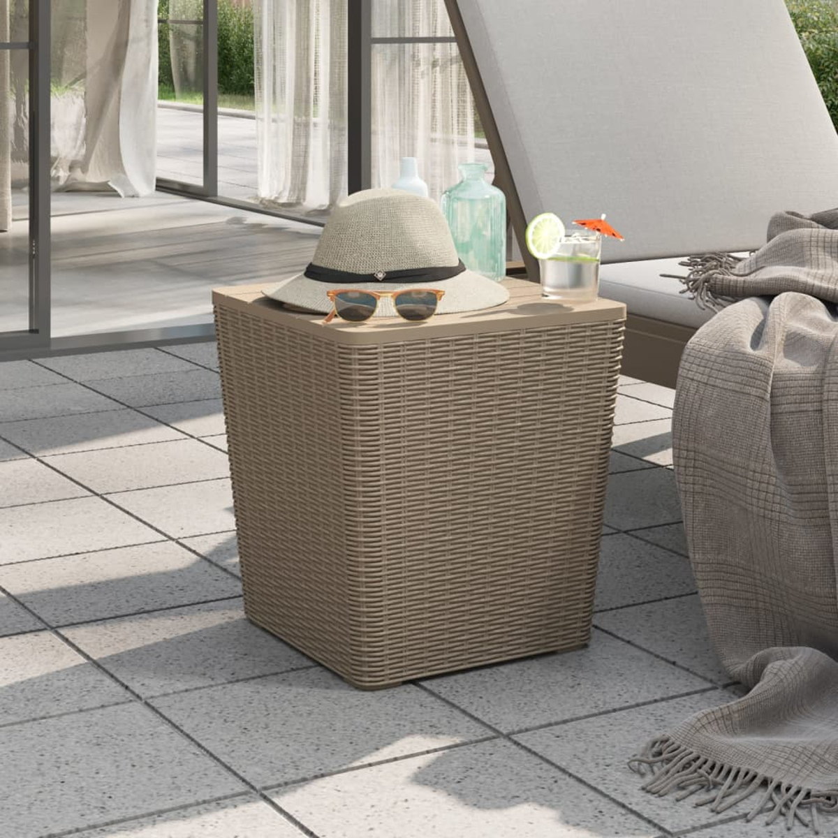 Beistelltisch aus Korbgeflecht mit Hut, Sonnenbrille und einem Getränk. Der Tisch steht auf einer Terrasse mit Liegestuhl.