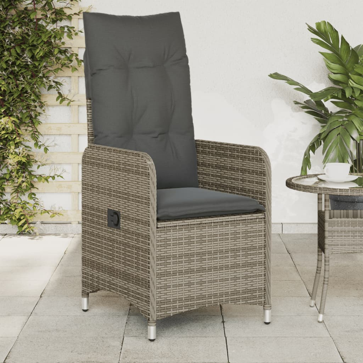Rattanstuhl mit grauem Kissen und Beistelltisch auf einer Terrasse.