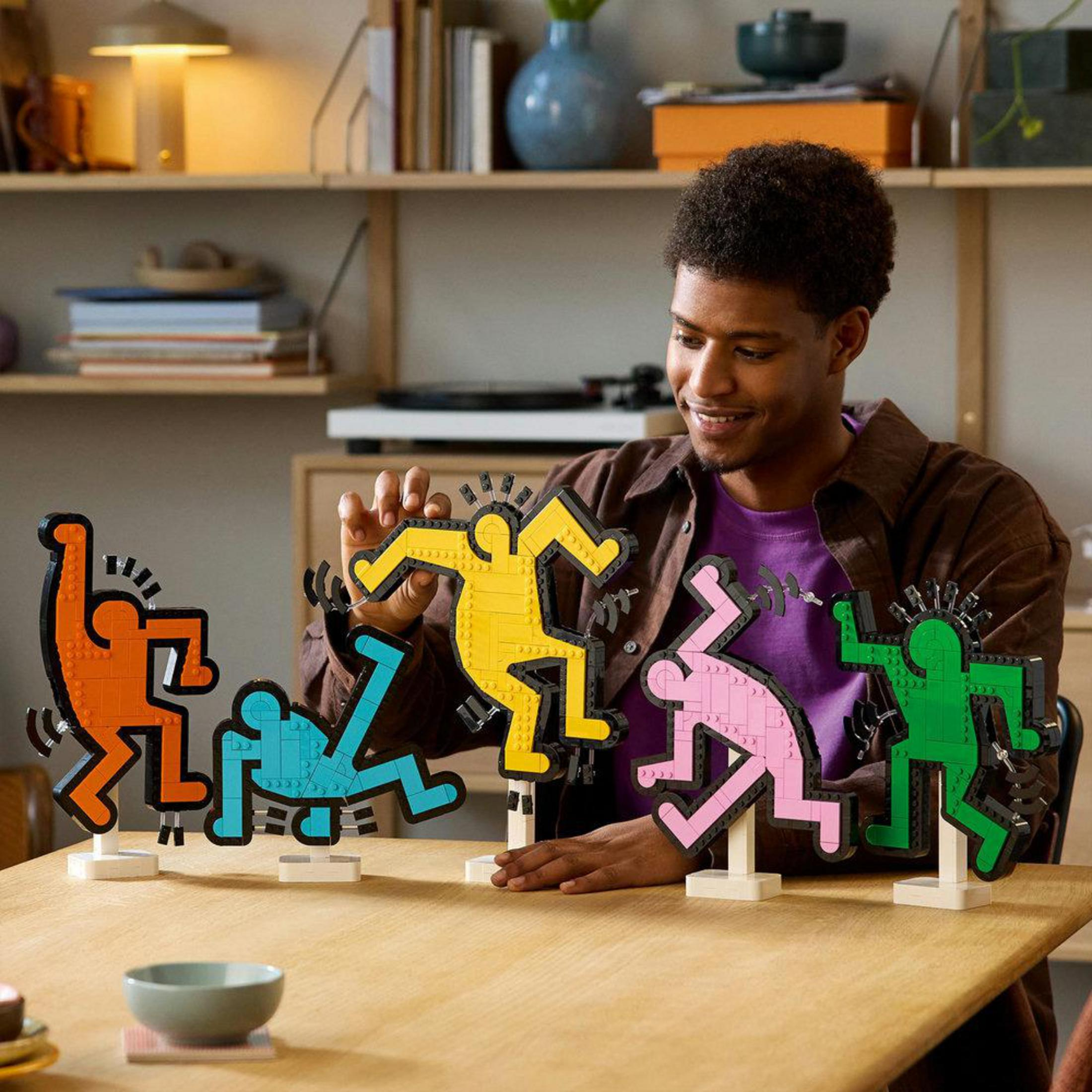 Un hombre con figuras de baile Lego. Las figuras son de diferentes colores, en una habitación.
