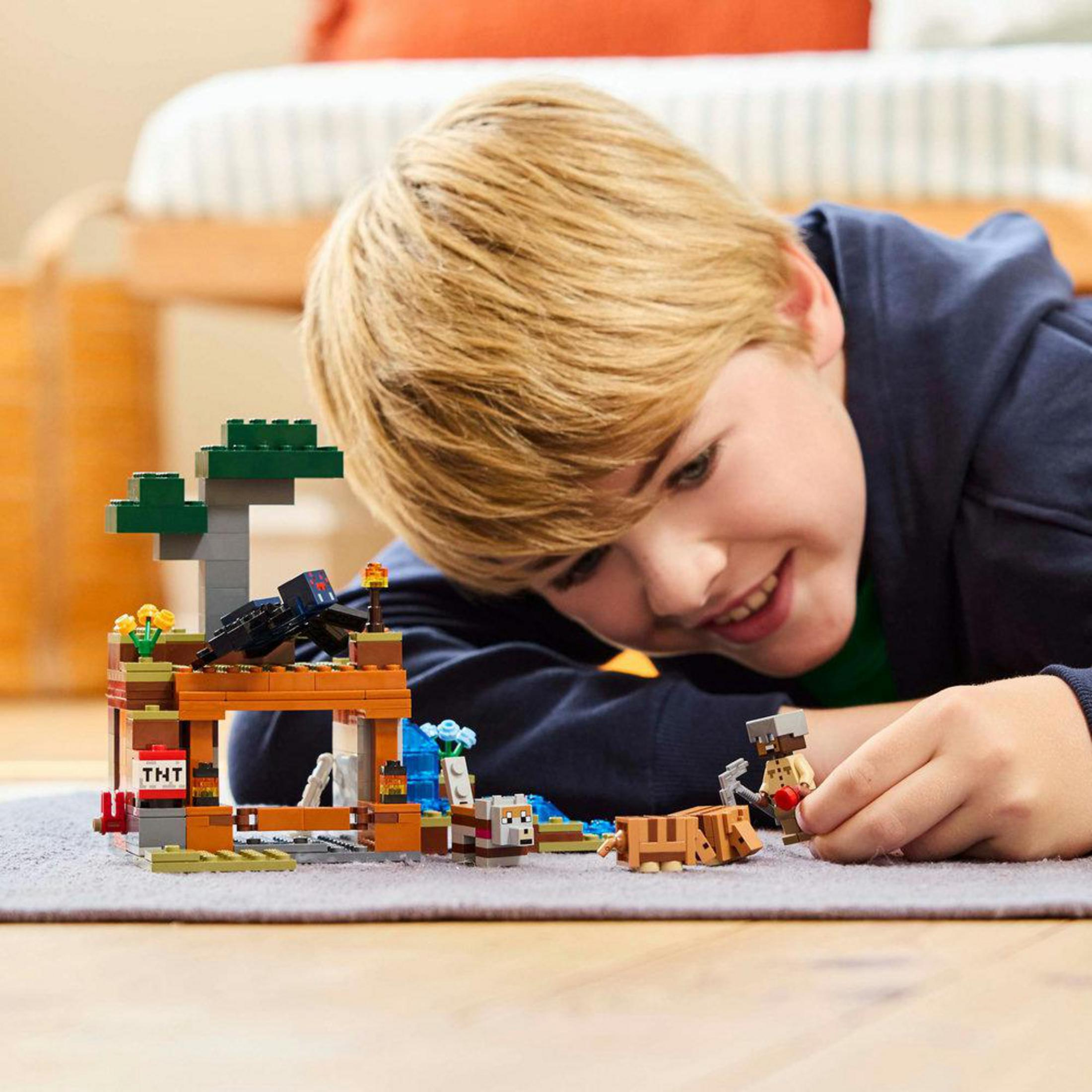 Chłopiec bawiący się zestawem LEGO Minecraft. Uśmiecha się i skupia na budynku i postaciach.