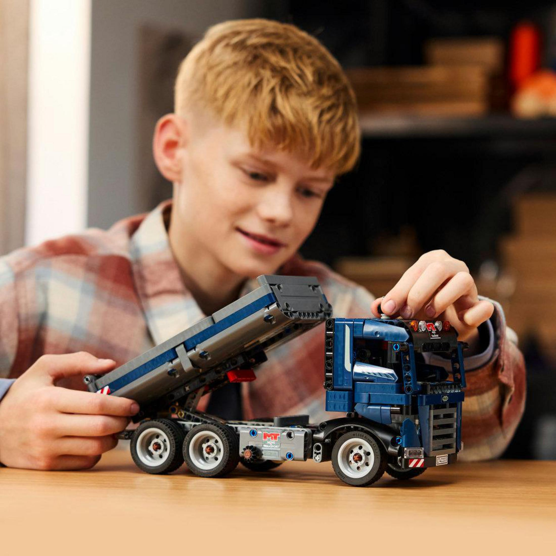Genç bir çocuk mavi bir Lego Technic Tipping Dump Truck modeliyle oynuyor.