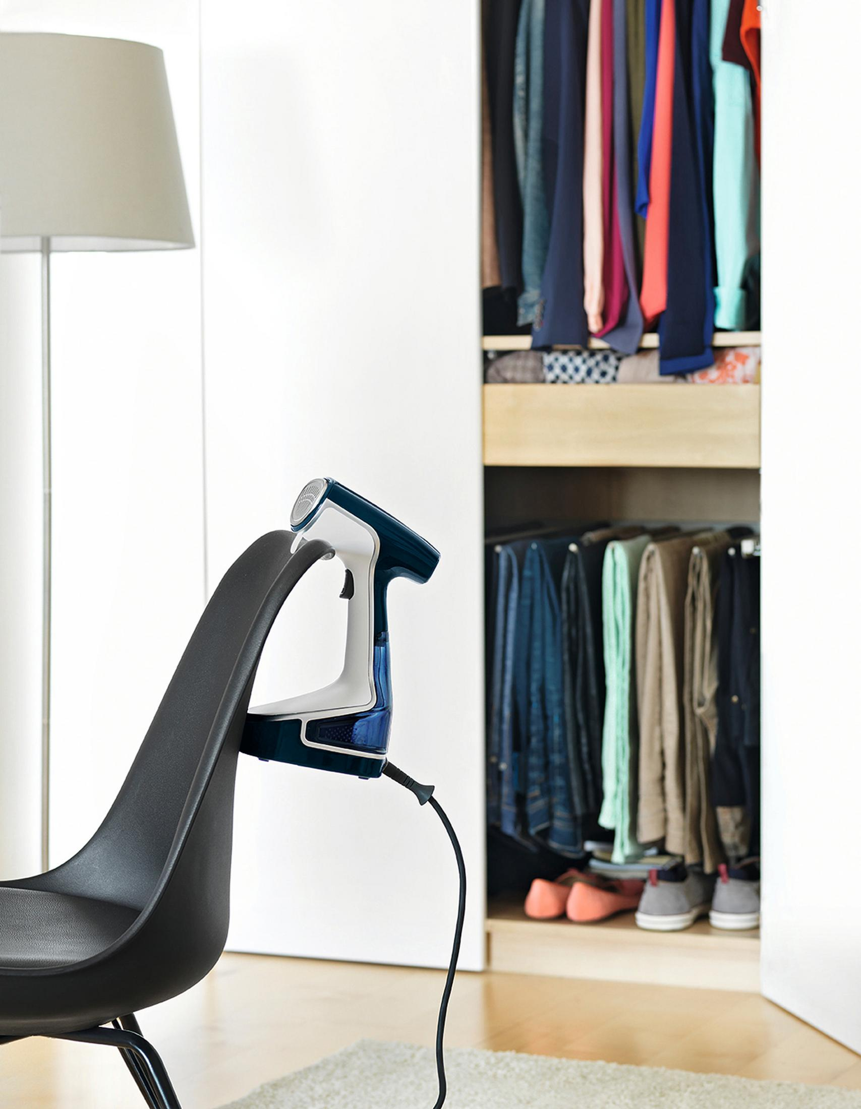 Vaporizador de mano en una silla negra, con ropa en un armario visible al fondo.