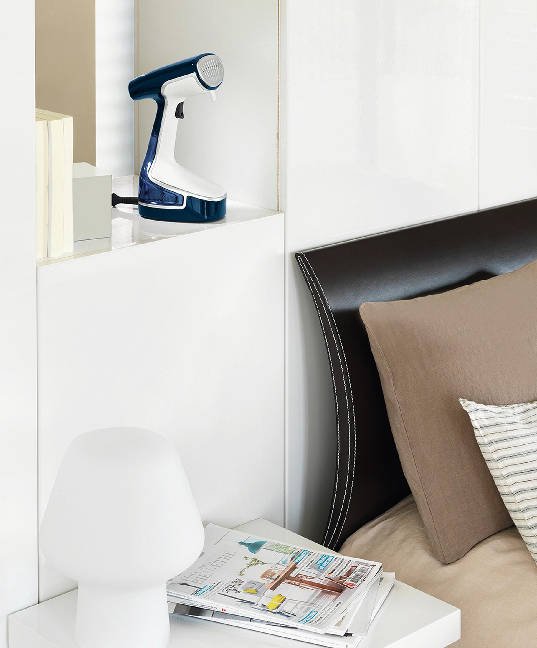 Un vaporizador en un estante blanco. Una lámpara, revistas y cama en el fondo.