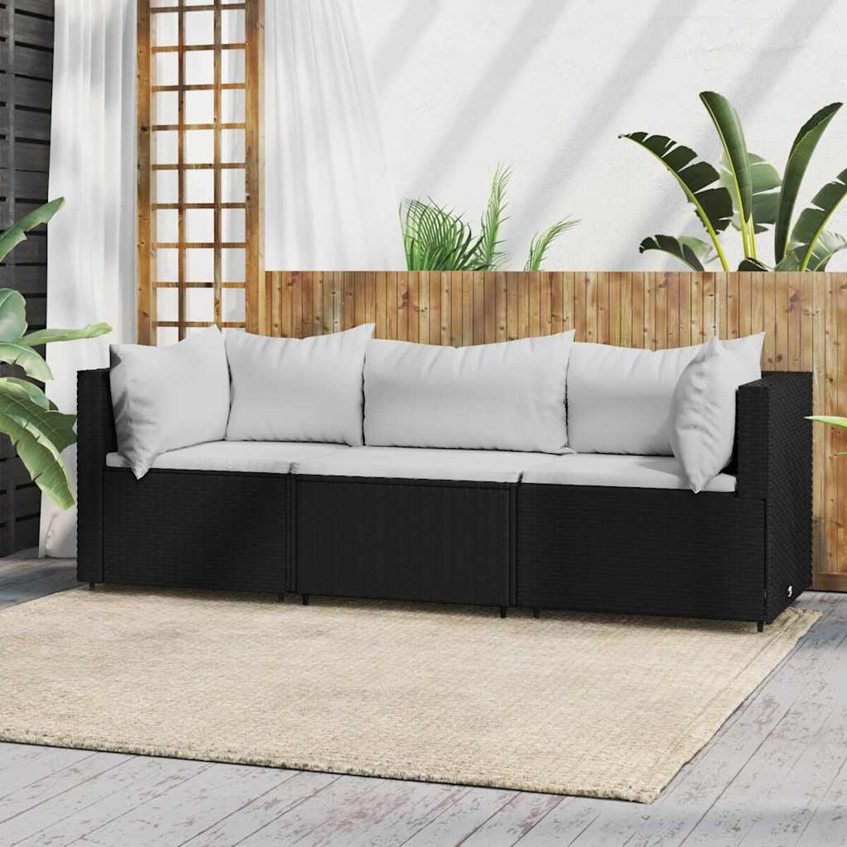 Ein schwarzes Korbmöbelsofa mit weißen Kissen und Kissen auf einem beigen Teppich. Palmen sind im Hintergrund.