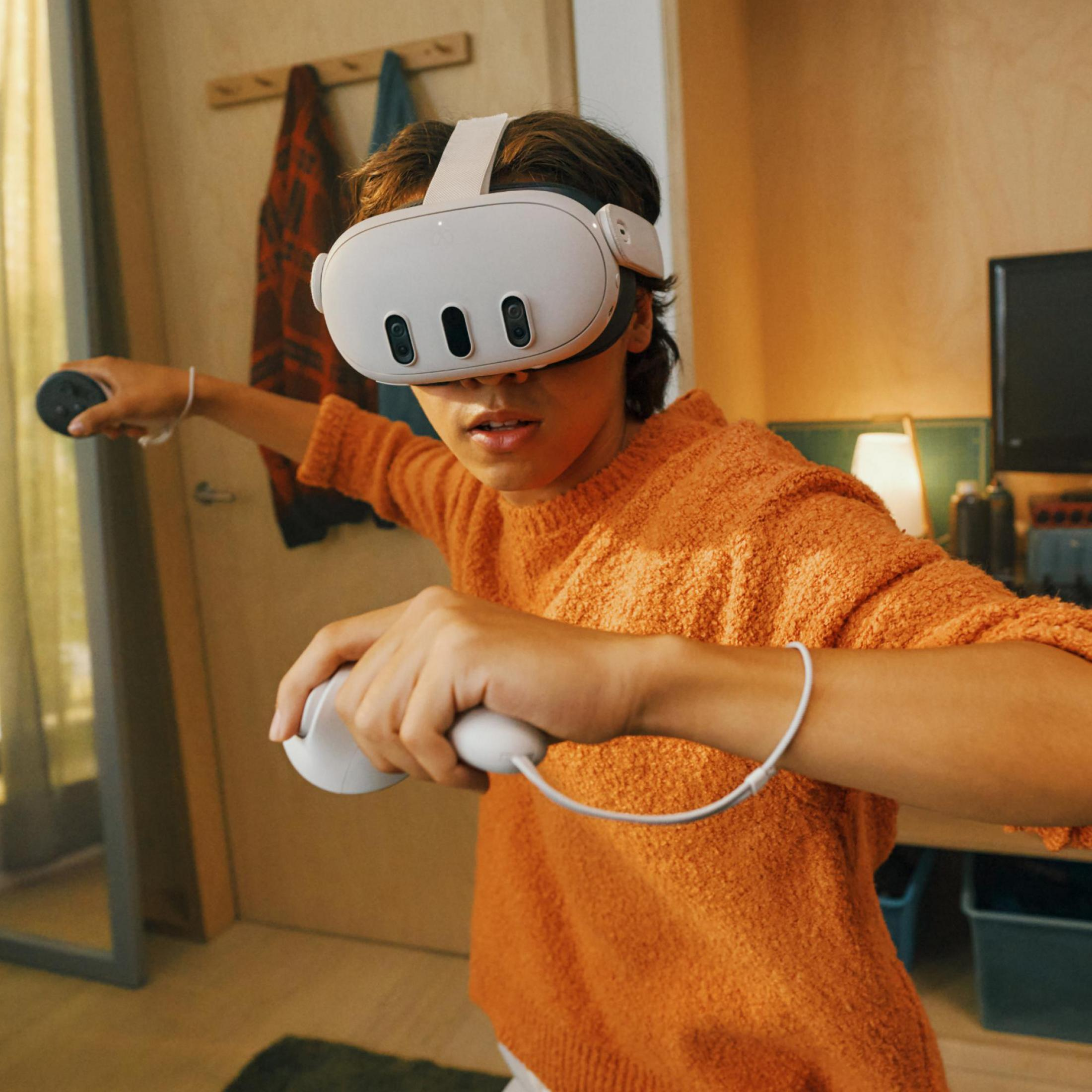 Osoba z zestawem VR i kontrolerami. Są w pokoju z łóżkiem i ubraniami.