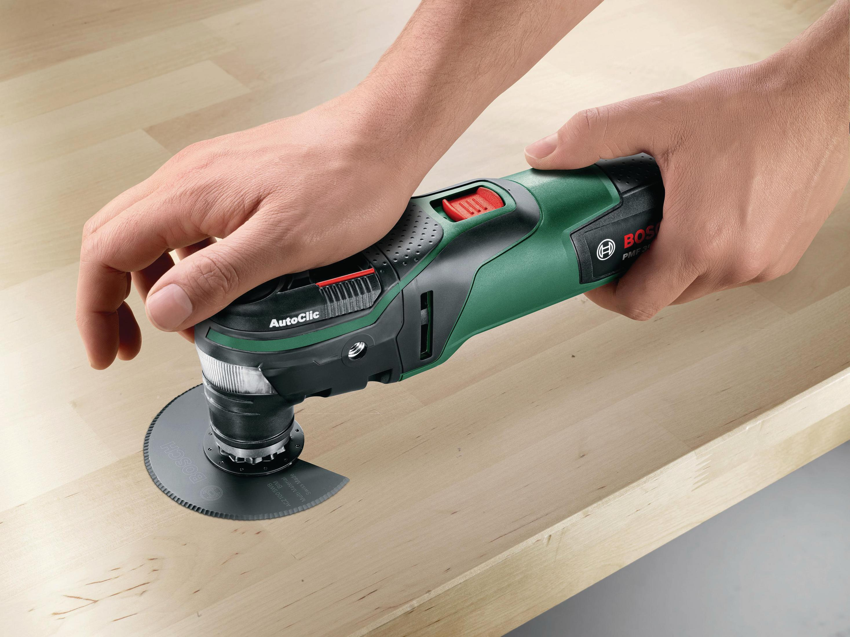 Une personne utilise un multi-outil Bosch sur une surface en bois, coupant un cercle.
