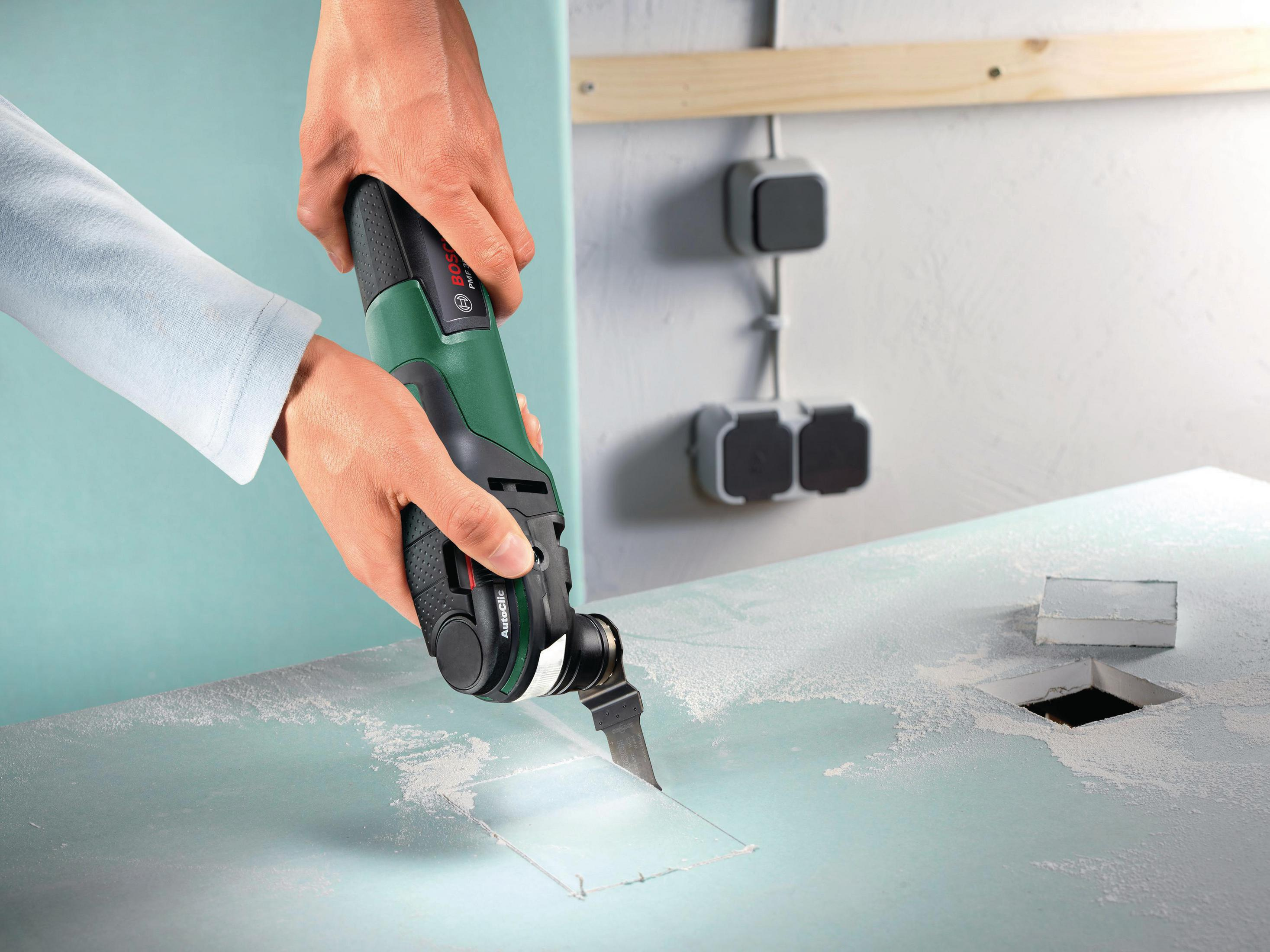 Une personne tenant un multi-outil Bosch coupant un trou dans une surface bleue.