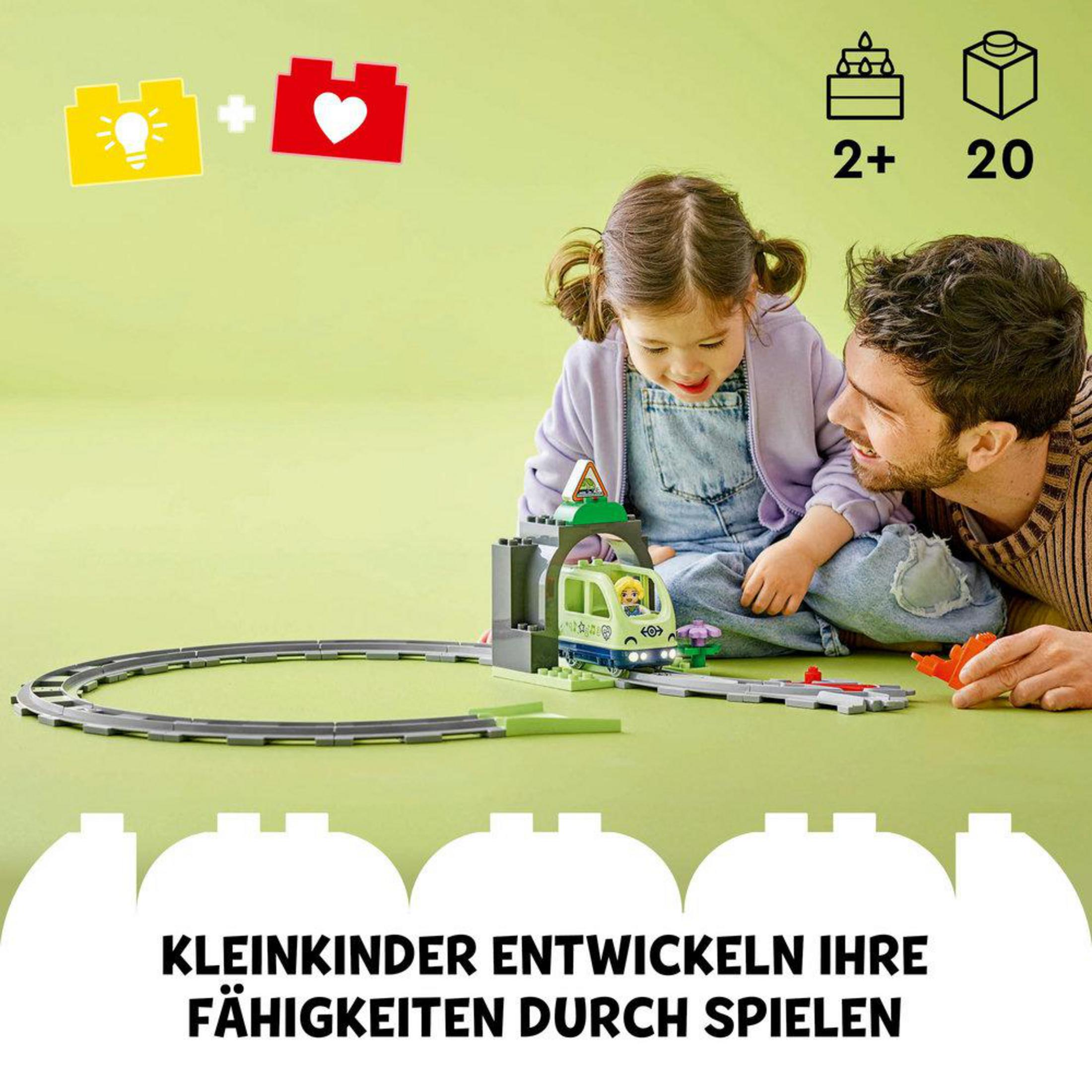 Dziewczynka i mężczyzna bawią się pociągiem-zabawką. Pociąg jest na torze. Tekst mówi 'KLEINKINDER ENTWICKELN IHRE FÄHIGKEITEN DURCH SPIELEN'.