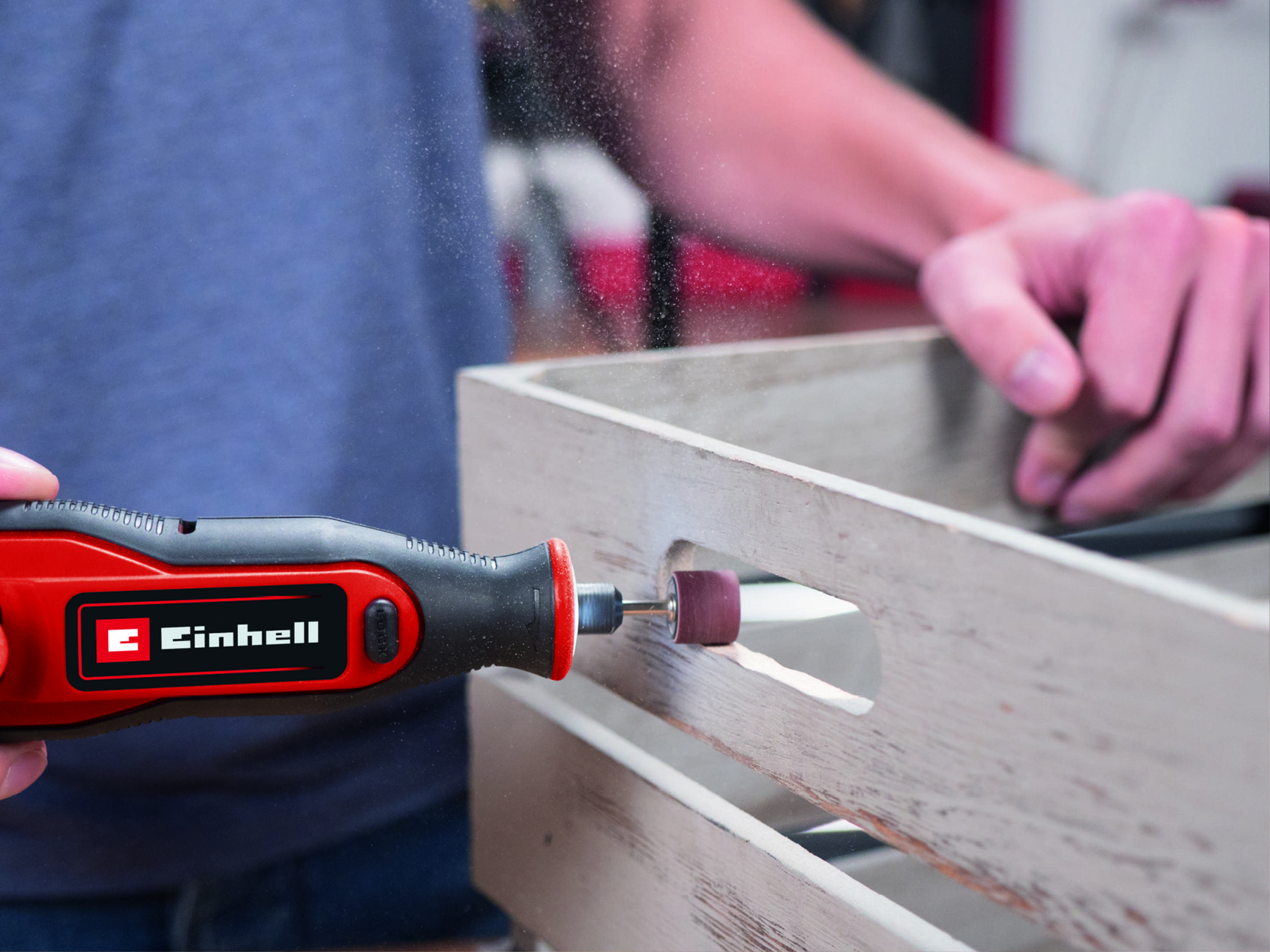 Eine Person benutzt ein rotes Elektrowerkzeug, um eine Holzkiste zu schleifen.