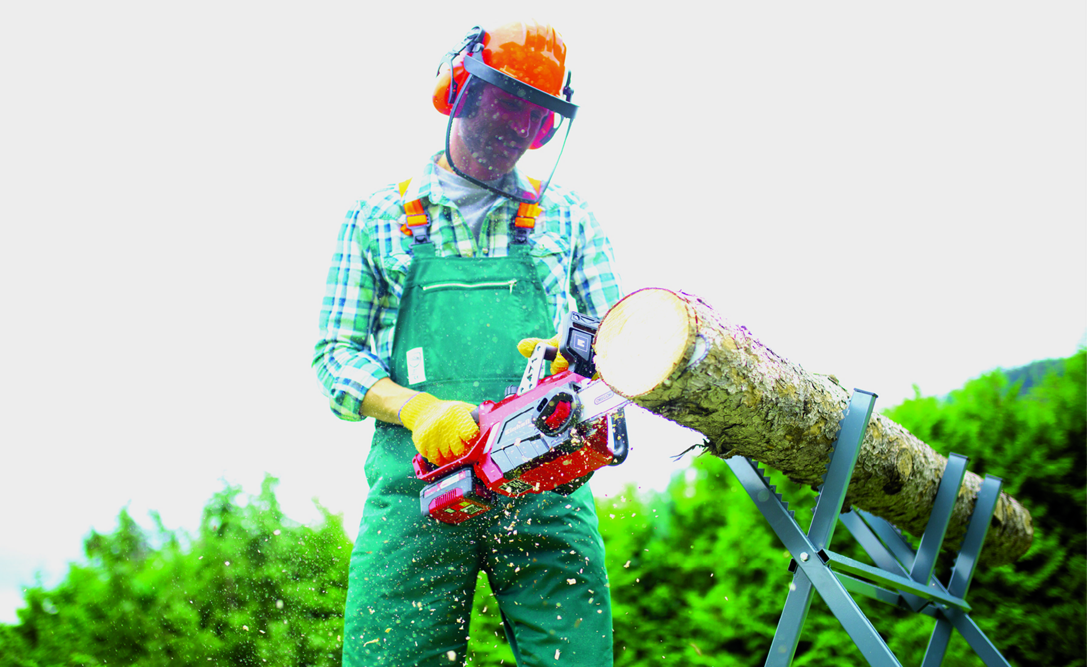 Mężczyzna używający czerwonej piły łańcuchowej do cięcia kłody na koziołku, w sprzęcie ochronnym.