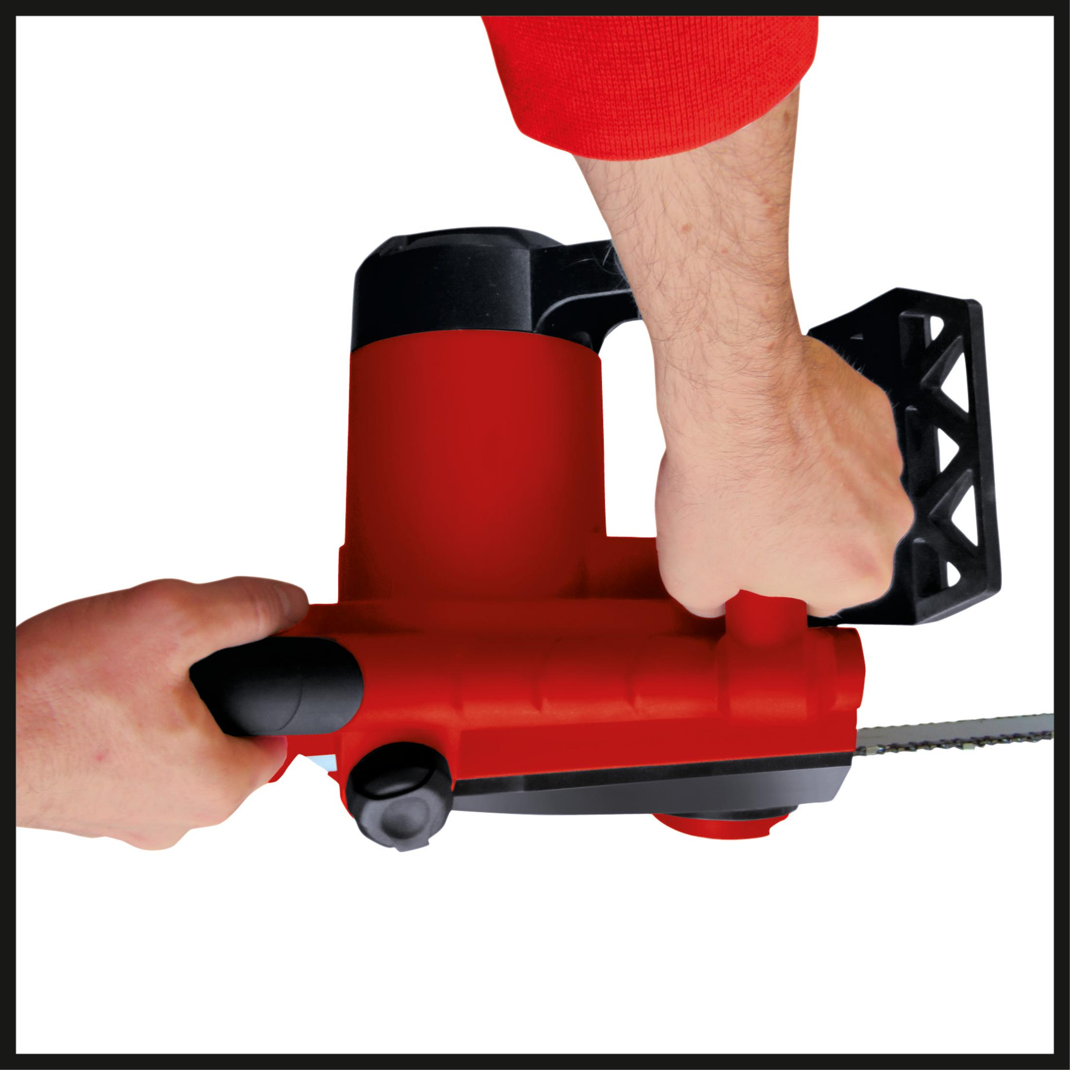 Ręce trzymające czerwono-czarną piłę łańcuchową. Osoba ma na sobie czerwoną koszulę z długim rękawem.