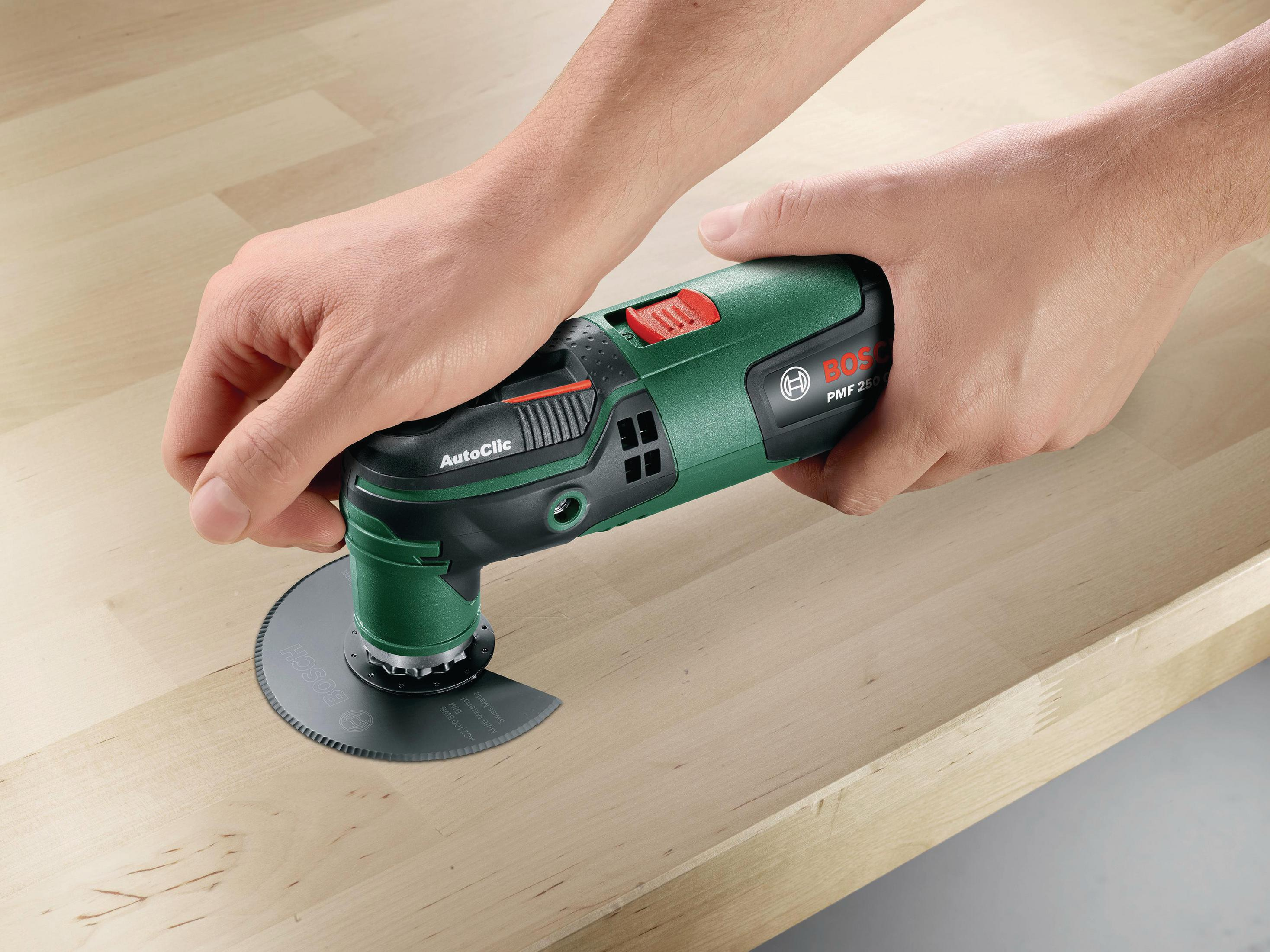 Mani che tengono un utensile elettrico verde e nero con una lama da taglio su una superficie di legno.