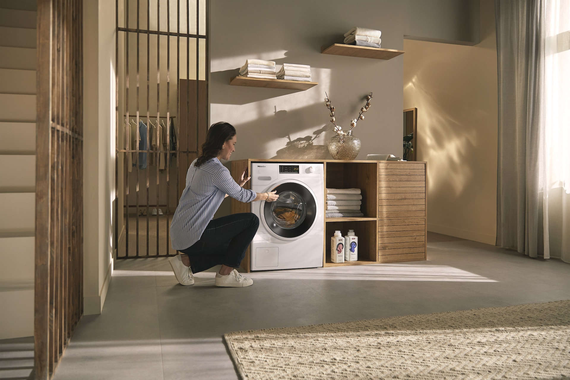 Frau interagiert mit einer weißen Waschmaschine. Moderne Waschküche mit Holzakzenten.