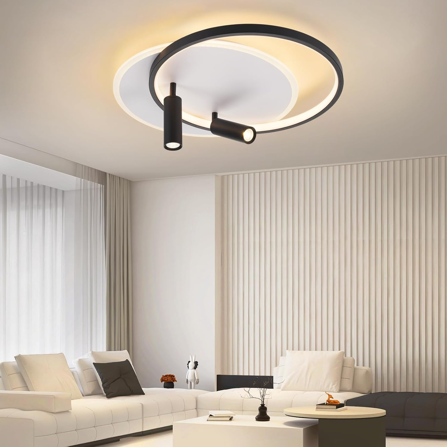 Un soggiorno con divano bianco, pareti bianche e una luce a soffitto con due faretti neri. Un vaso nero è su un tavolo.
