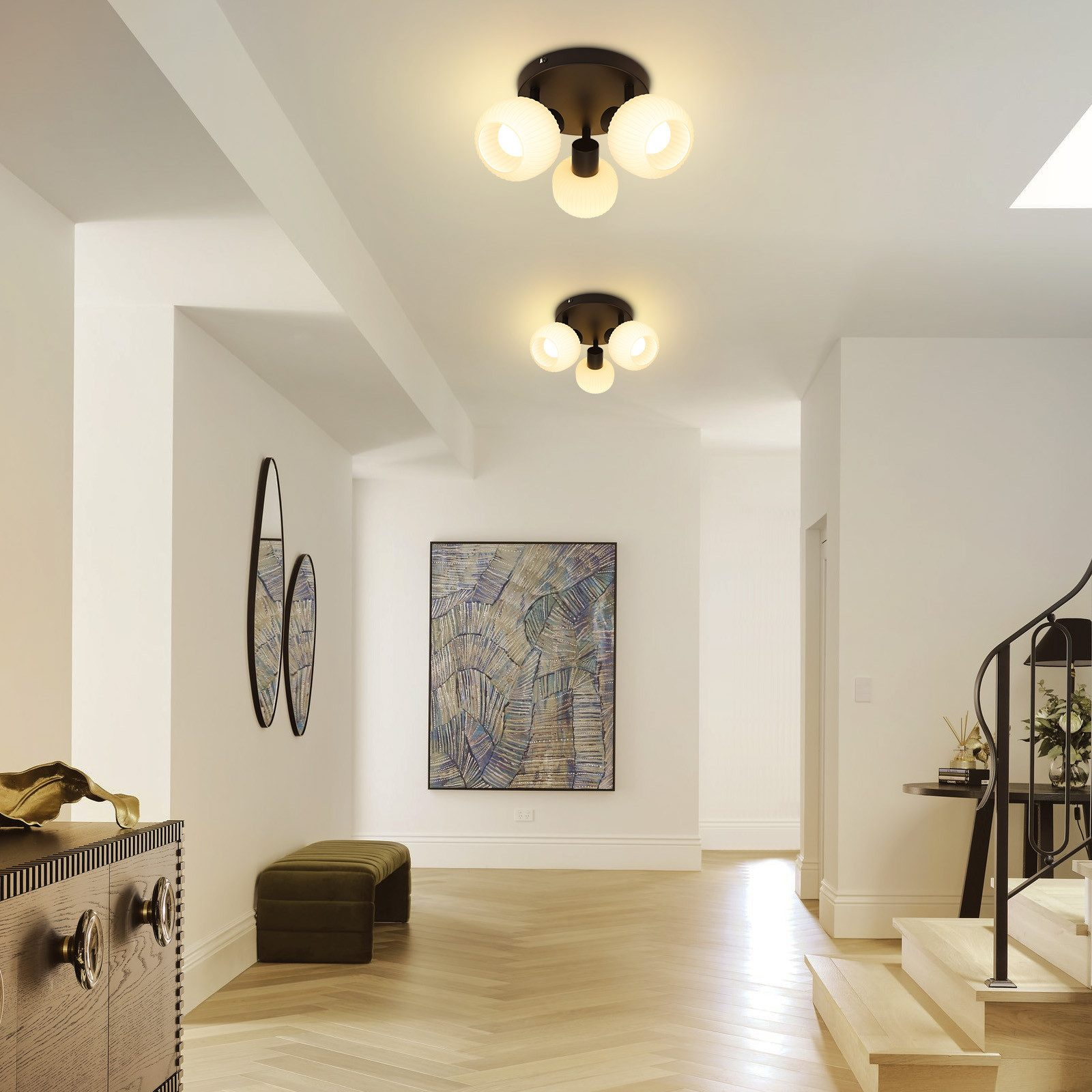 Corridoio con pareti bianche, pavimento in legno e due lampade a soffitto con paralumi in vetro.