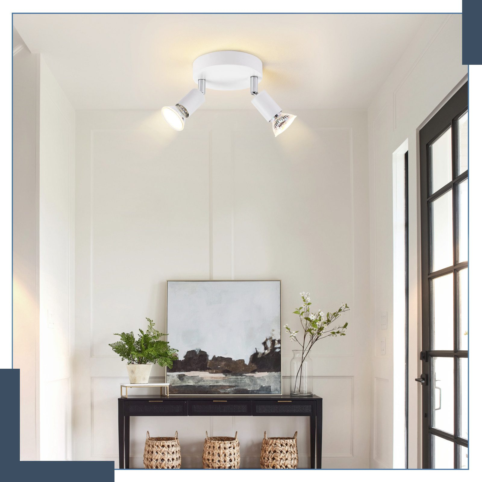 Una lampada da soffitto bianca con due faretti, un tavolo con decorazioni e un dipinto sulla parete.