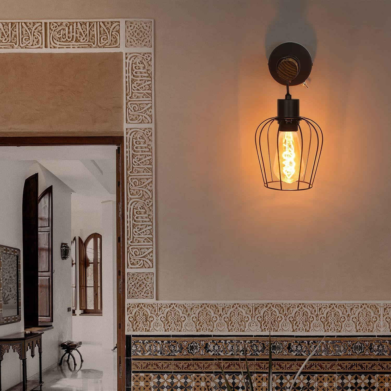Lampada da parete con cornice nera e design a gabbia attorno a una lampadina a vista. Lo sfondo è beige.