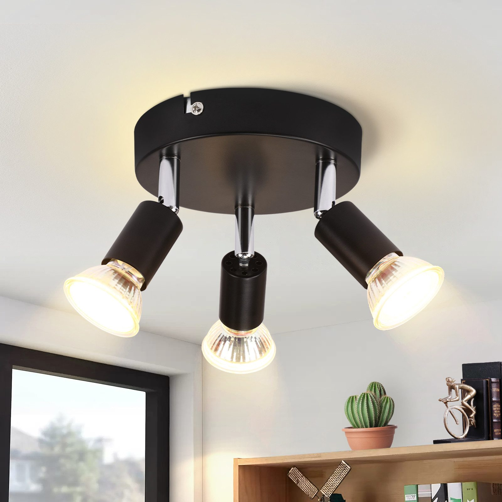 Una lampada da soffitto nera con tre luci. Una mensola con decorazioni è visibile in primo piano.