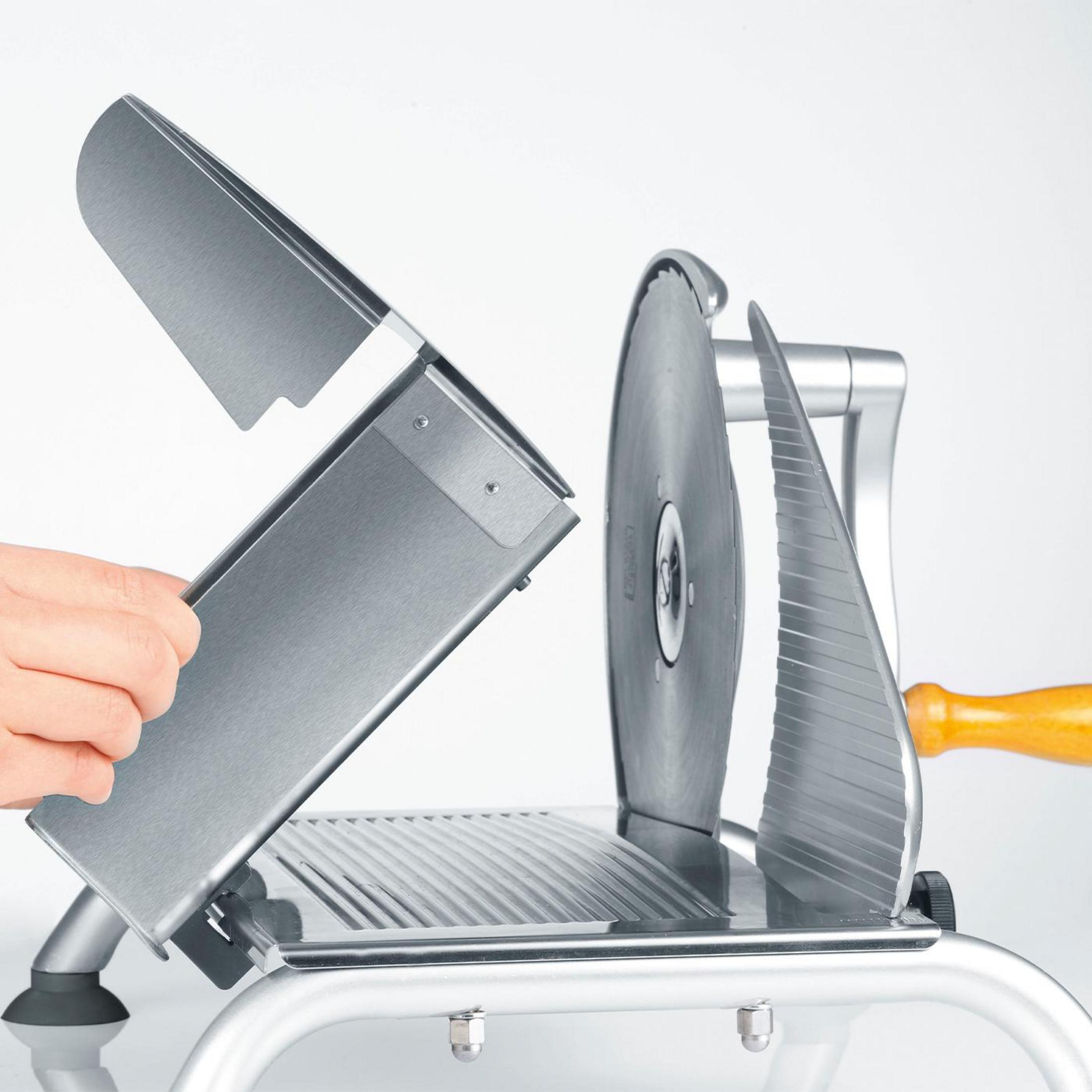 Osoba trzymająca element krajalnicy do mięsa. Krajalnica jest srebrna i ma drewniany uchwyt.