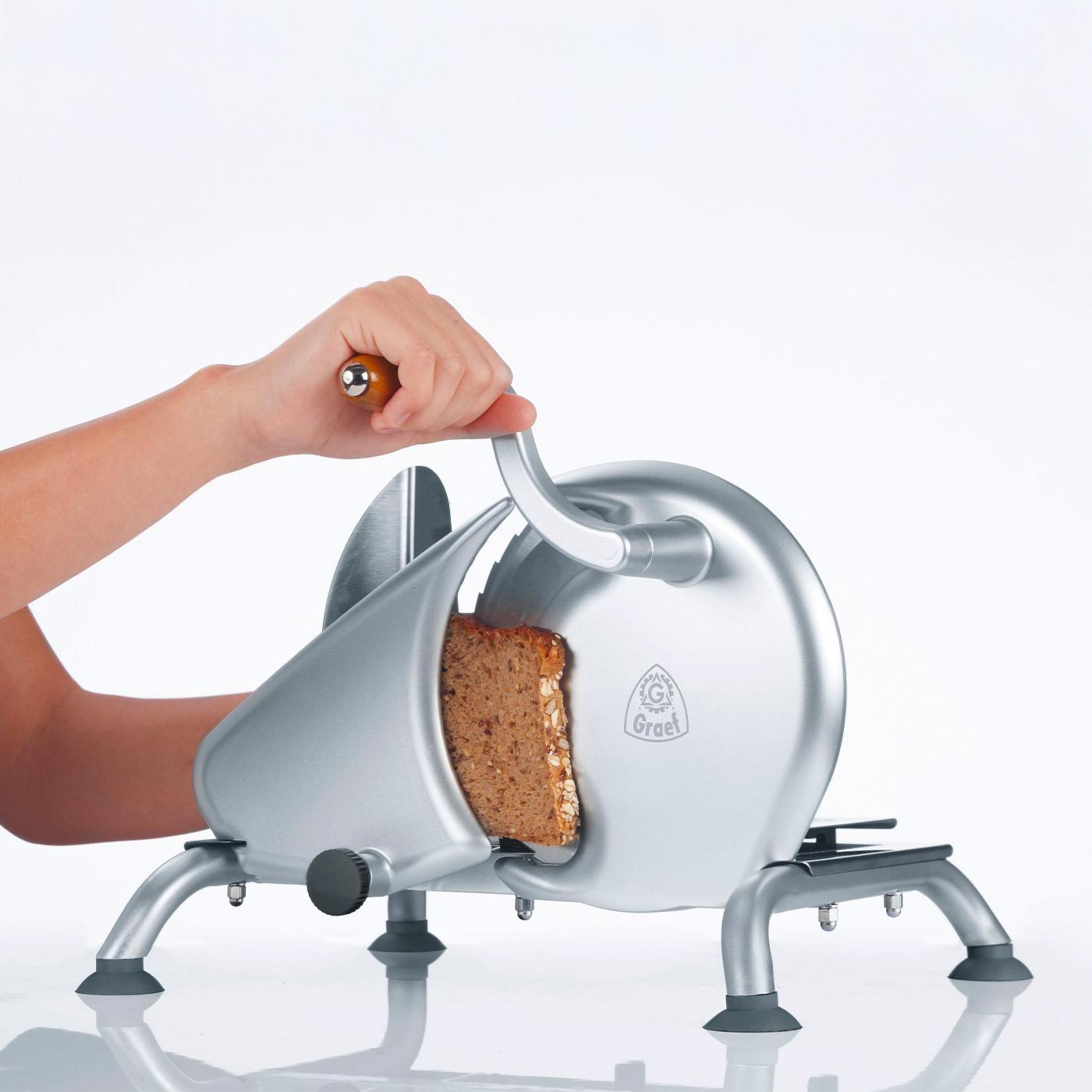 Ręka kroi chleb srebrną krajalnicą do chleba. Chleb jest brązowy, a tło białe.