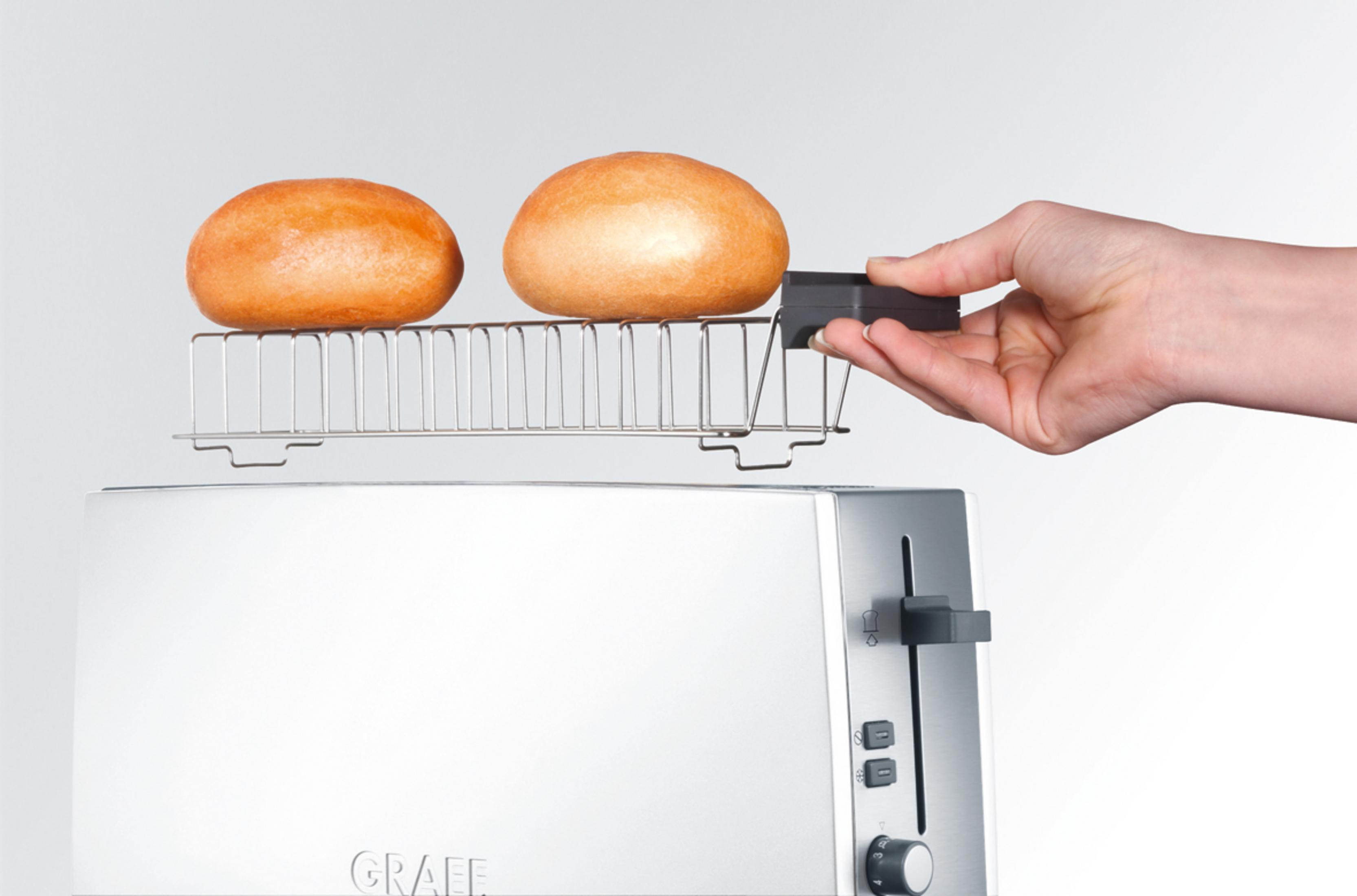 Eine Hand, die ein Gestell mit zwei Brötchen hält. Im Hintergrund ein weißer Toaster.