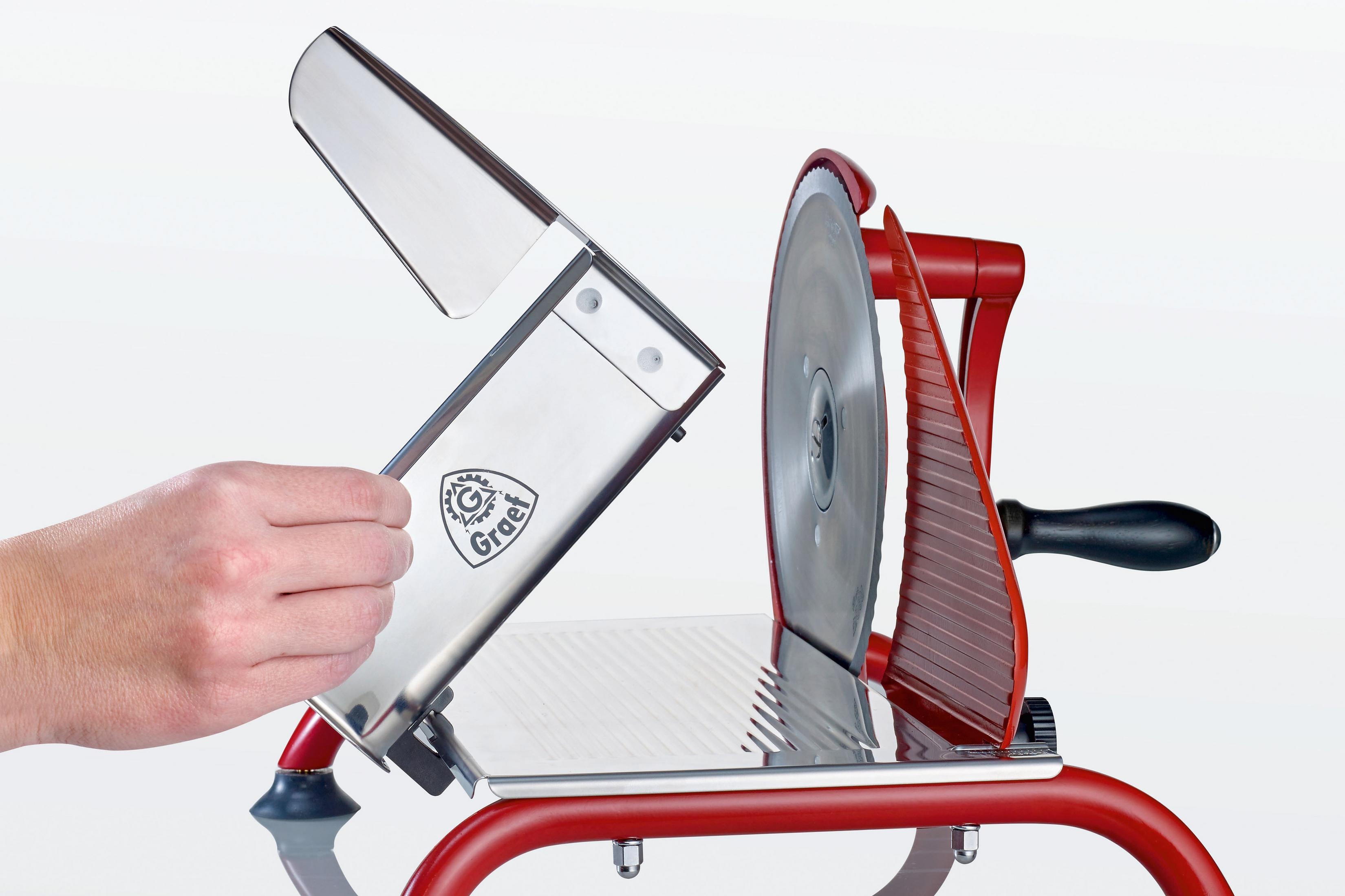 Eine rote Fleischschneidemaschine mit silberner Klinge und einer Hand, die sie bedient.