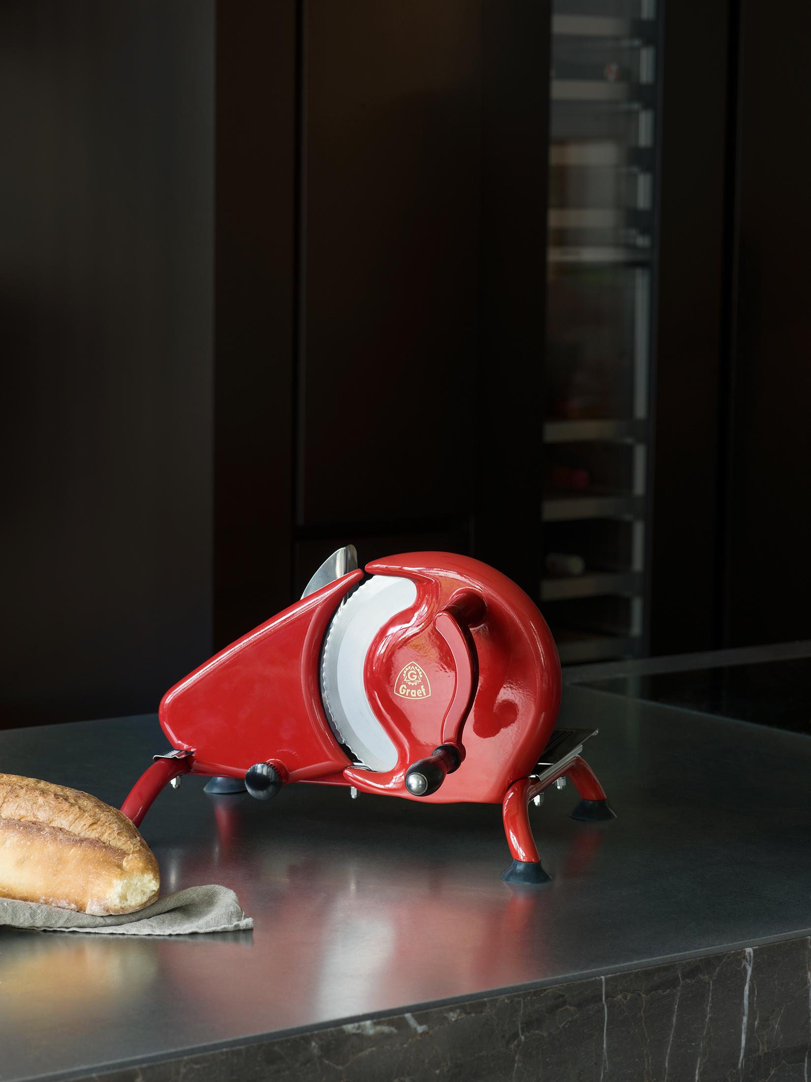 Ein roter Schneider mit einem Brotlaib auf einer Theke, vor dunklem Hintergrund.