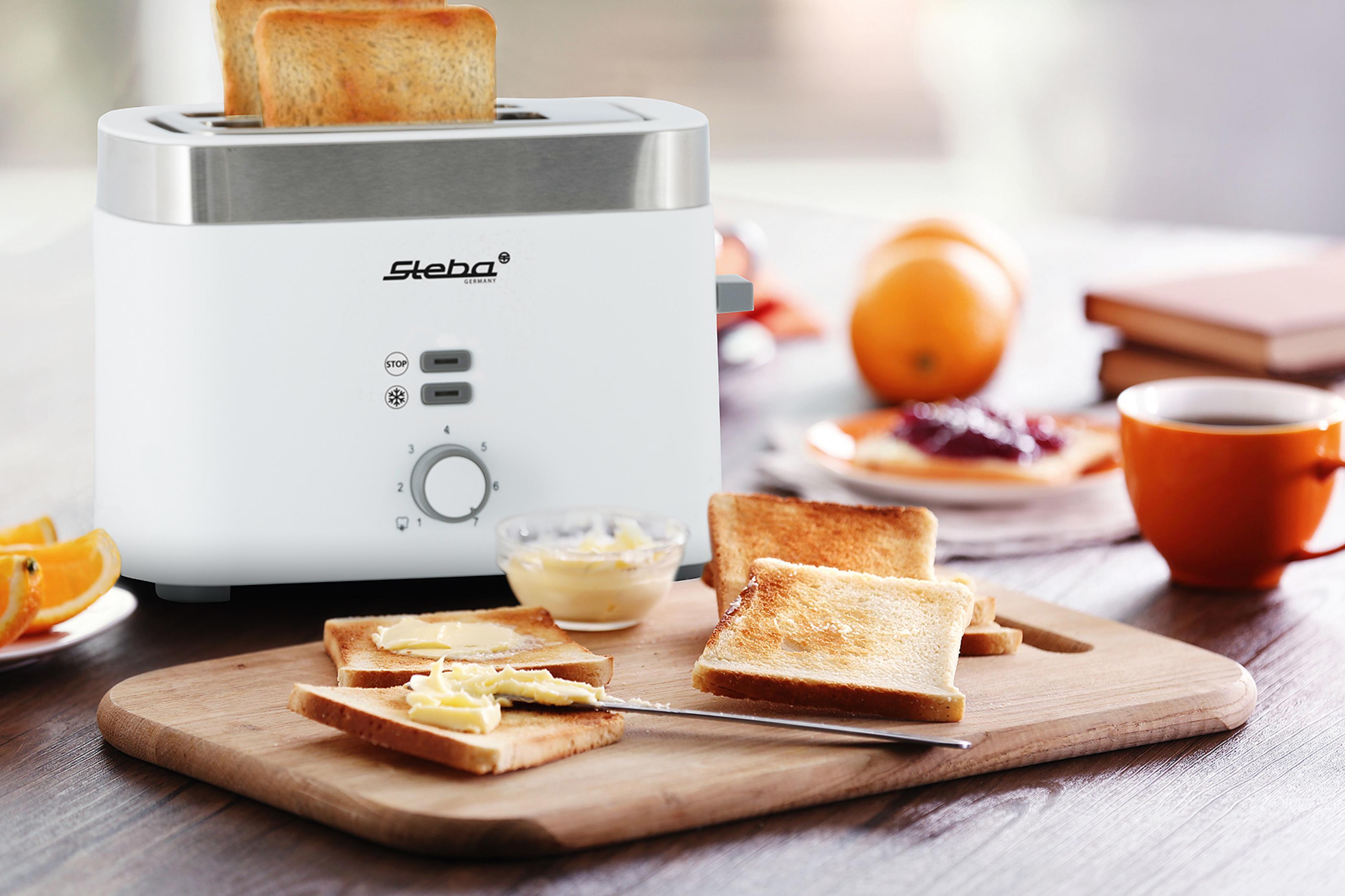 Ein weißer Toaster mit Toast, Butter und Orangen auf einem Holzbrett.