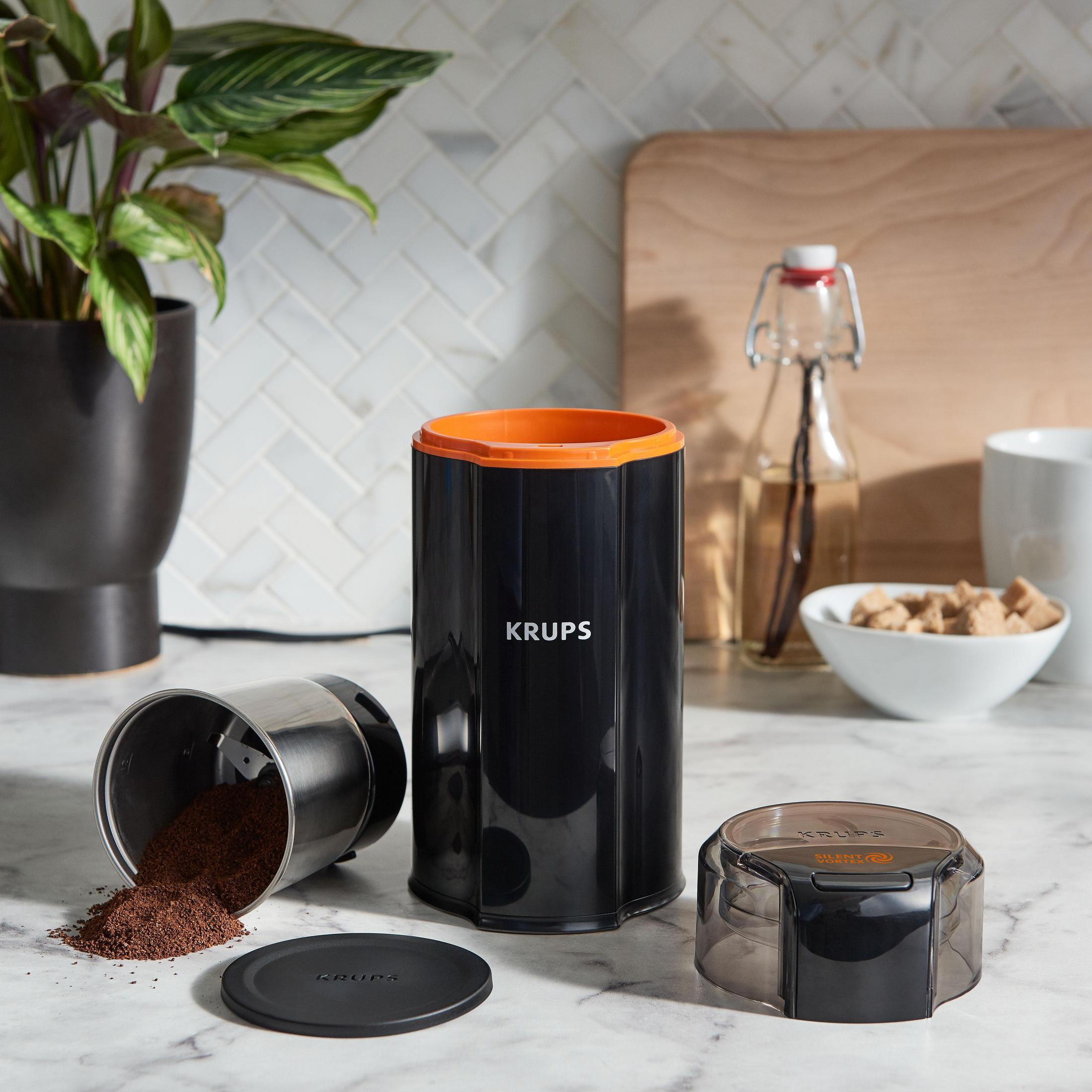 Młynek do kawy z fusami. Czarna i pomarańczowa podstawa, pojemnik ze stali nierdzewnej, przezroczysta pokrywa.