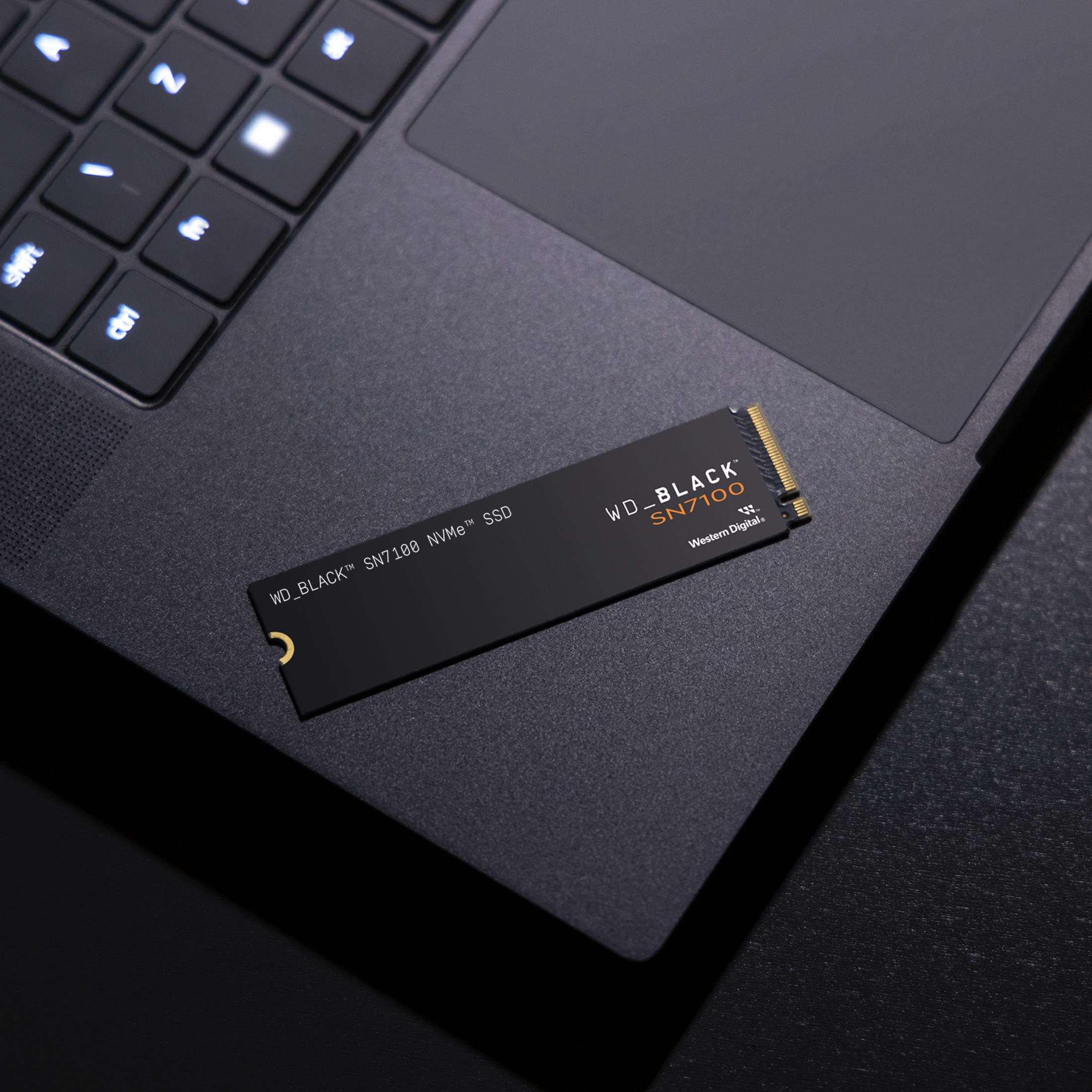 SSD NVMe WD_BLACK SN7100 nero su superficie laptop nera, con luci.