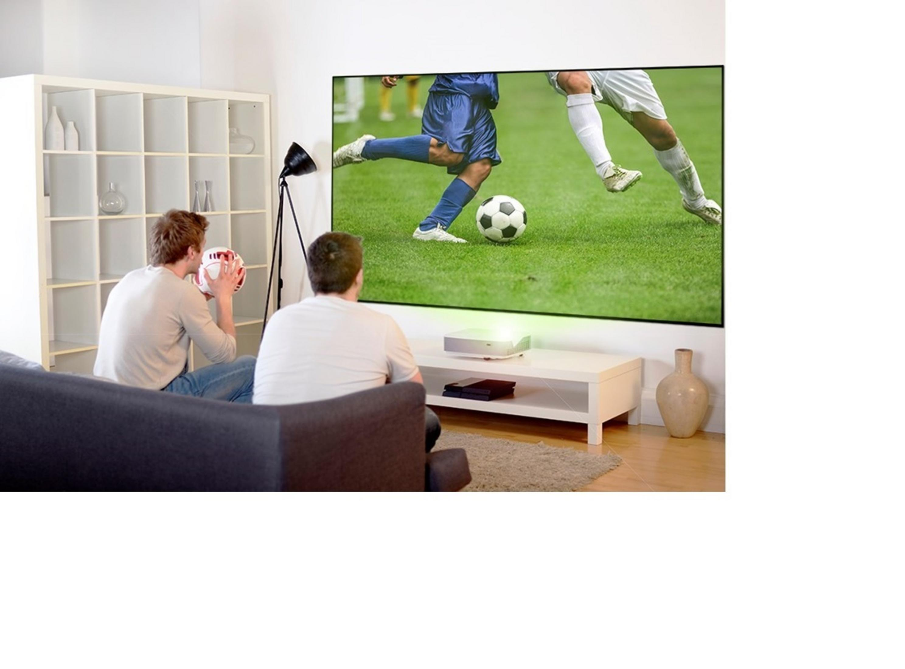 Dos hombres viendo un partido de fútbol proyectado en una pantalla grande en un salón.