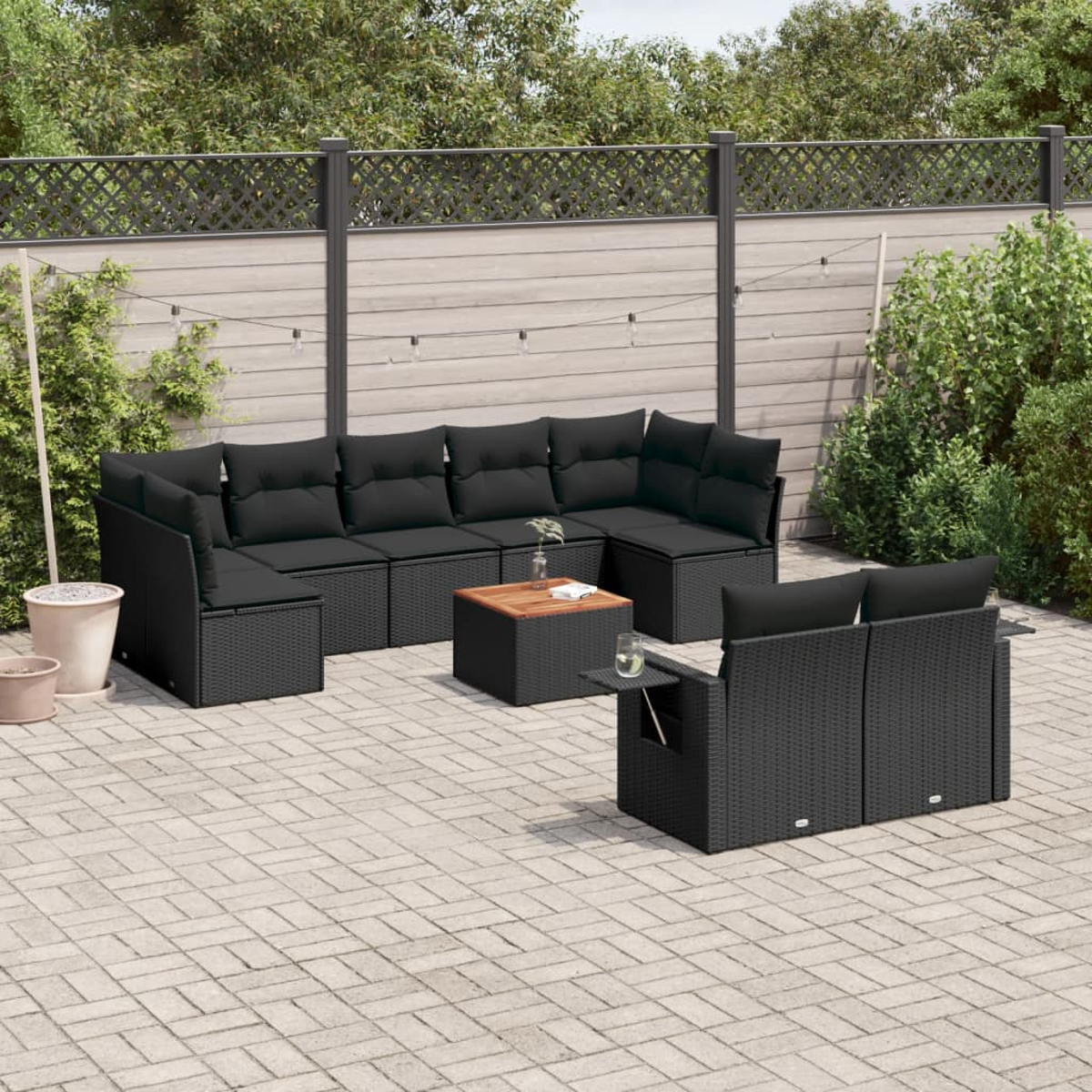 Set di mobili da esterno in rattan nero su un patio pavimentato. Include un divano componibile, un tavolino e un tavolino laterale.