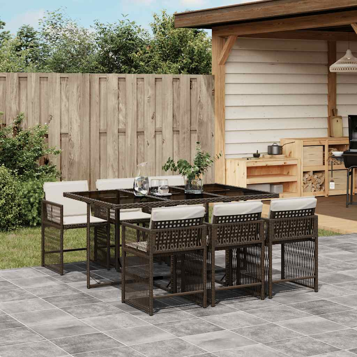 Set da pranzo in vimini marrone scuro, con tavolo in vetro, su un patio piastrellato, ambiente esterno.
