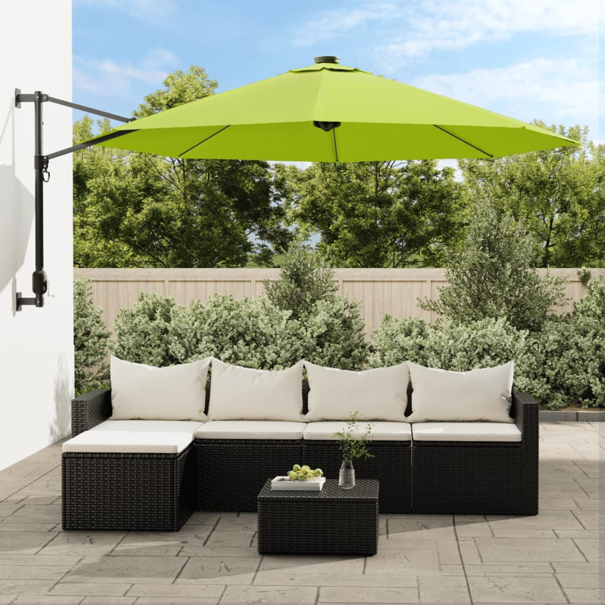 Außenbereich mit einem schwarzen Sofa und einem grünen Sonnenschirm. Es gibt einen Tisch und einen Garten.
