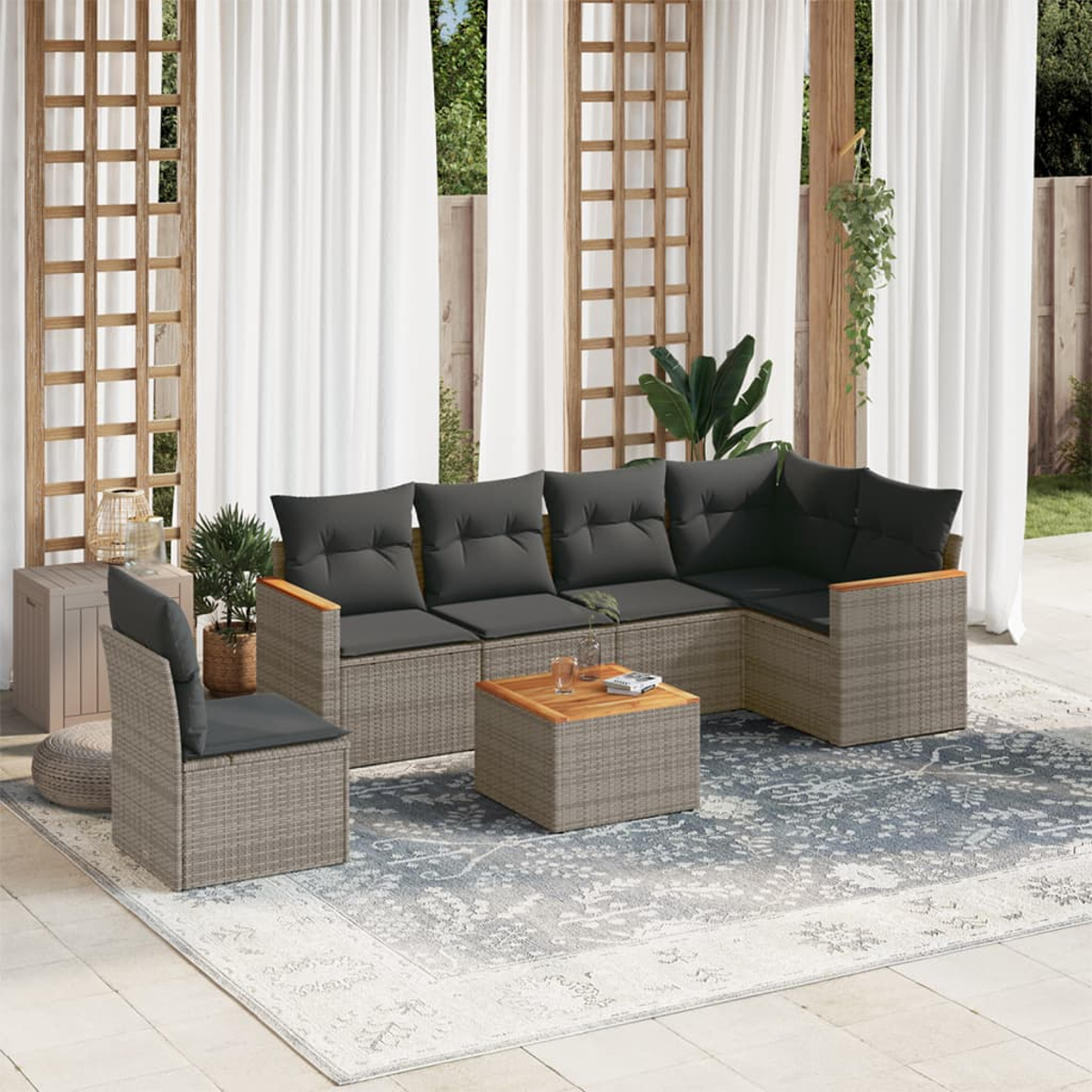 Terrassenset mit grauem Rattan, dunkelgrauen Kissen, Tisch und gemustertem Teppich.
