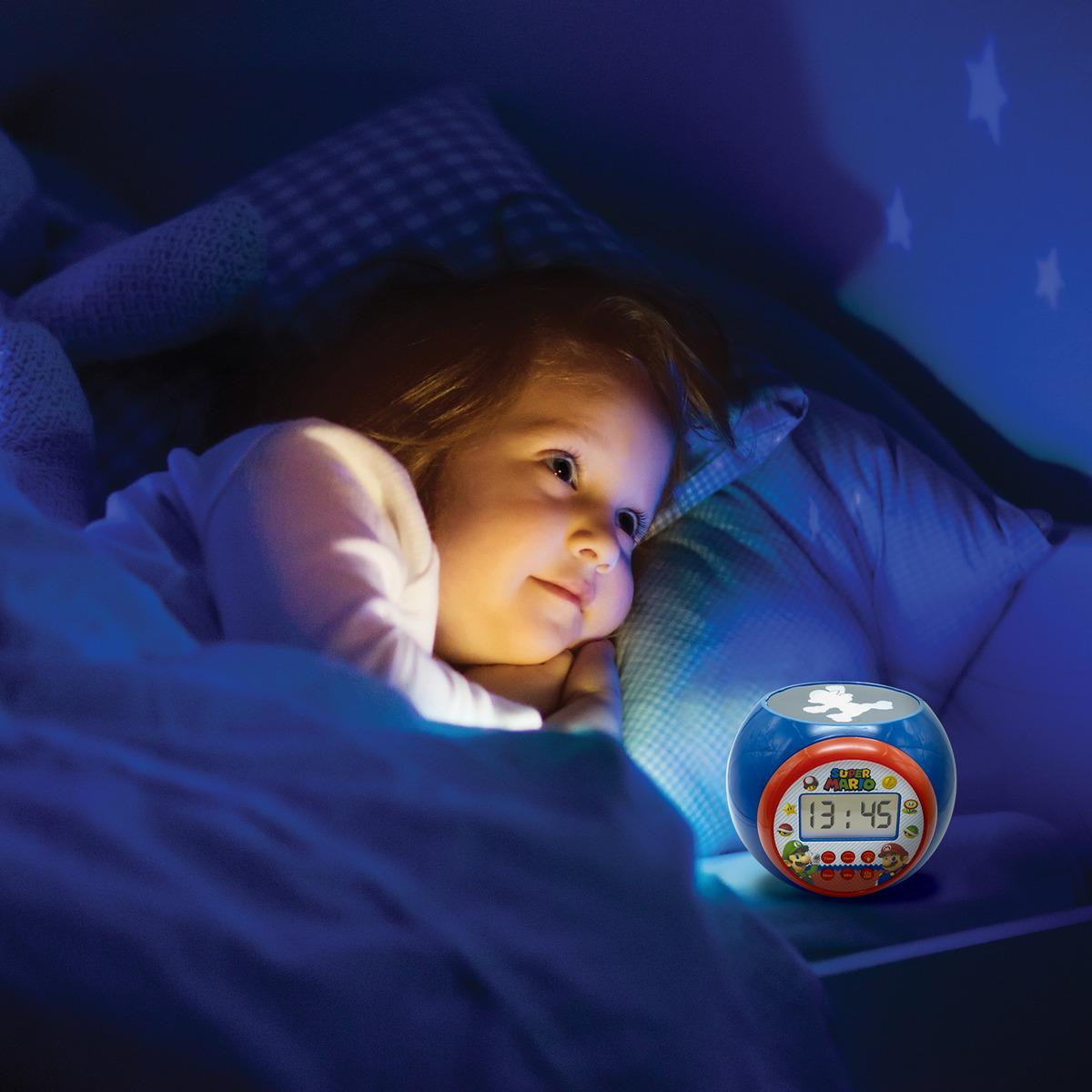 Niño pequeño en la cama mirando un despertador de Super Mario. El reloj tiene un diseño azul y rojo.